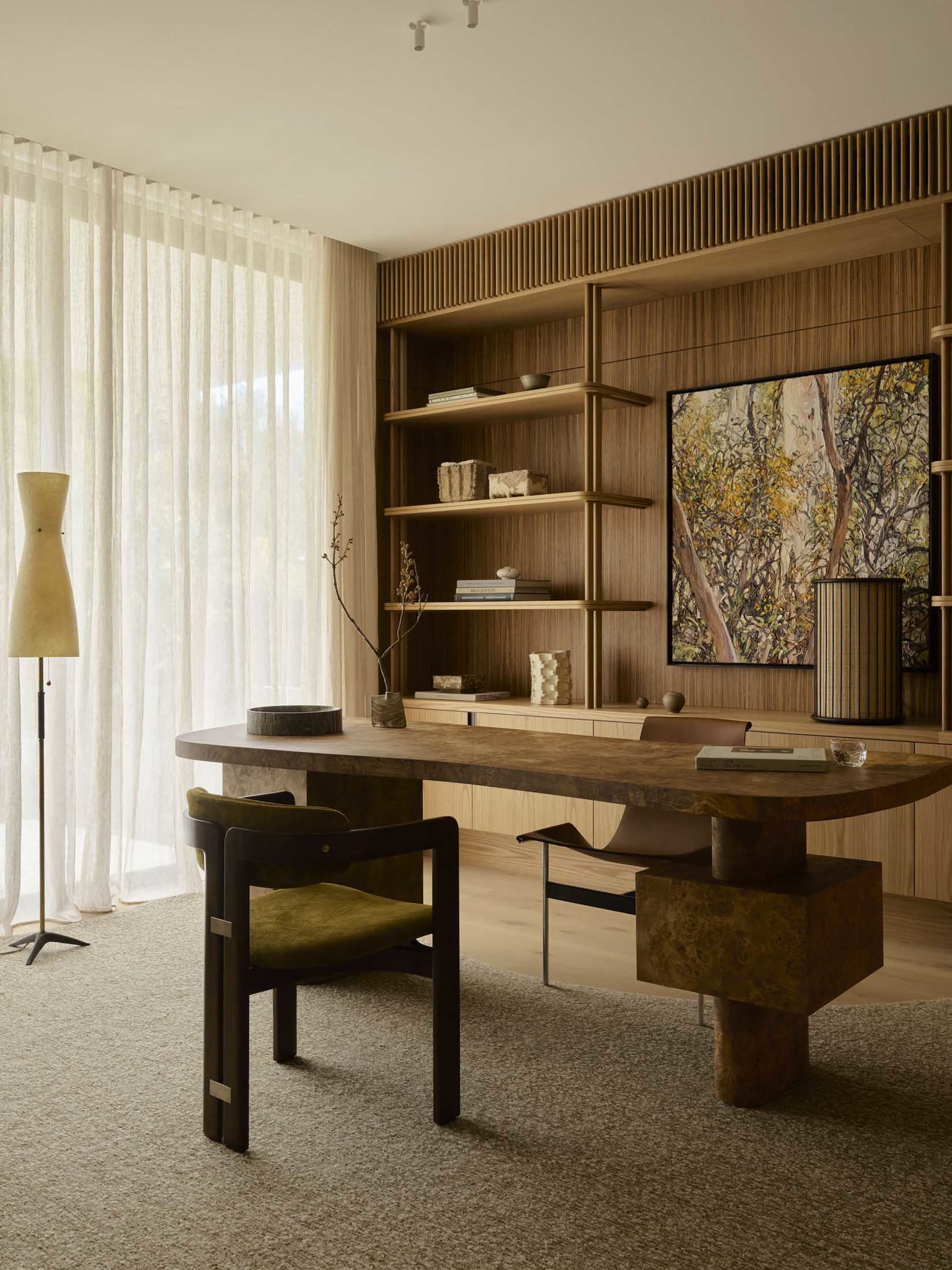 A modern home office featuring a wooden desk and shelving unit with decorative items and a large artwork.