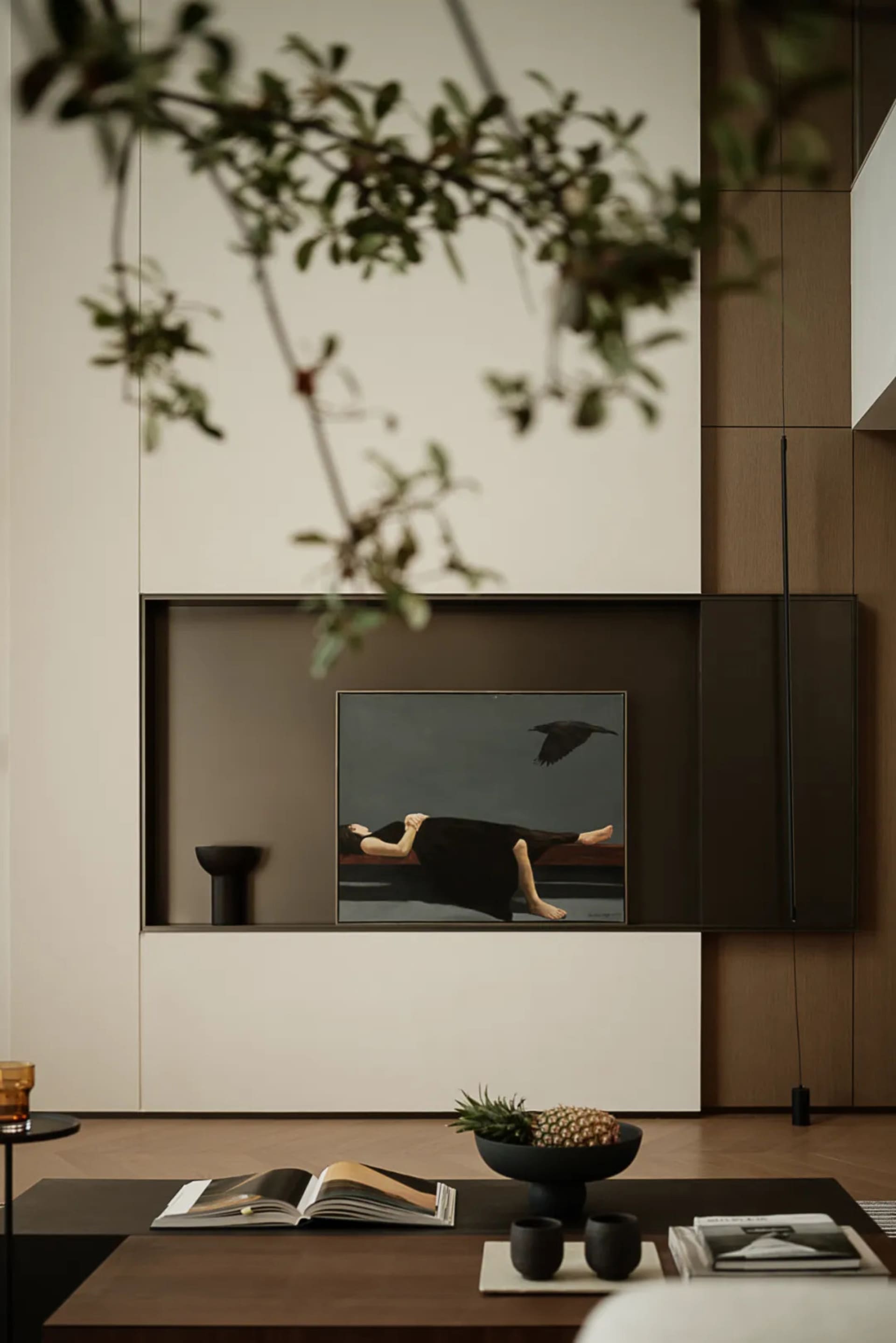 A modern minimalist living room with simple decor, a wooden floor, a black coffee table, and a large wall-mounted artwork fea