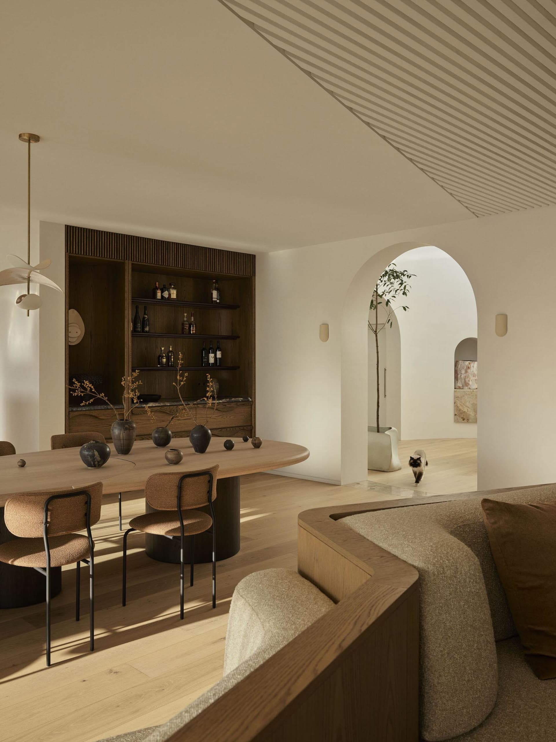 A modern minimalist living room with wood finishes, featuring a curved sofa, a wooden dining table, and a wooden shelving uni