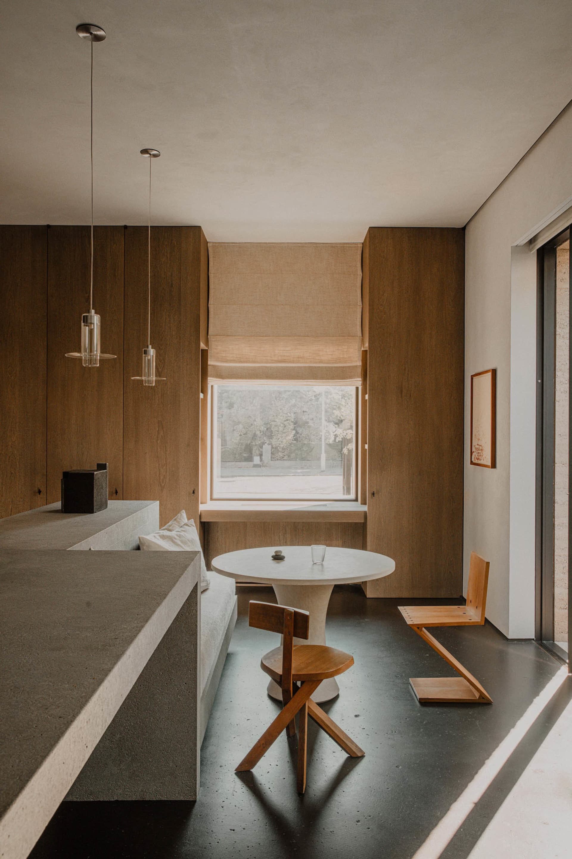 A modern residential kitchen with a concrete countertop and wooden accents, featuring a small dining area with a round white