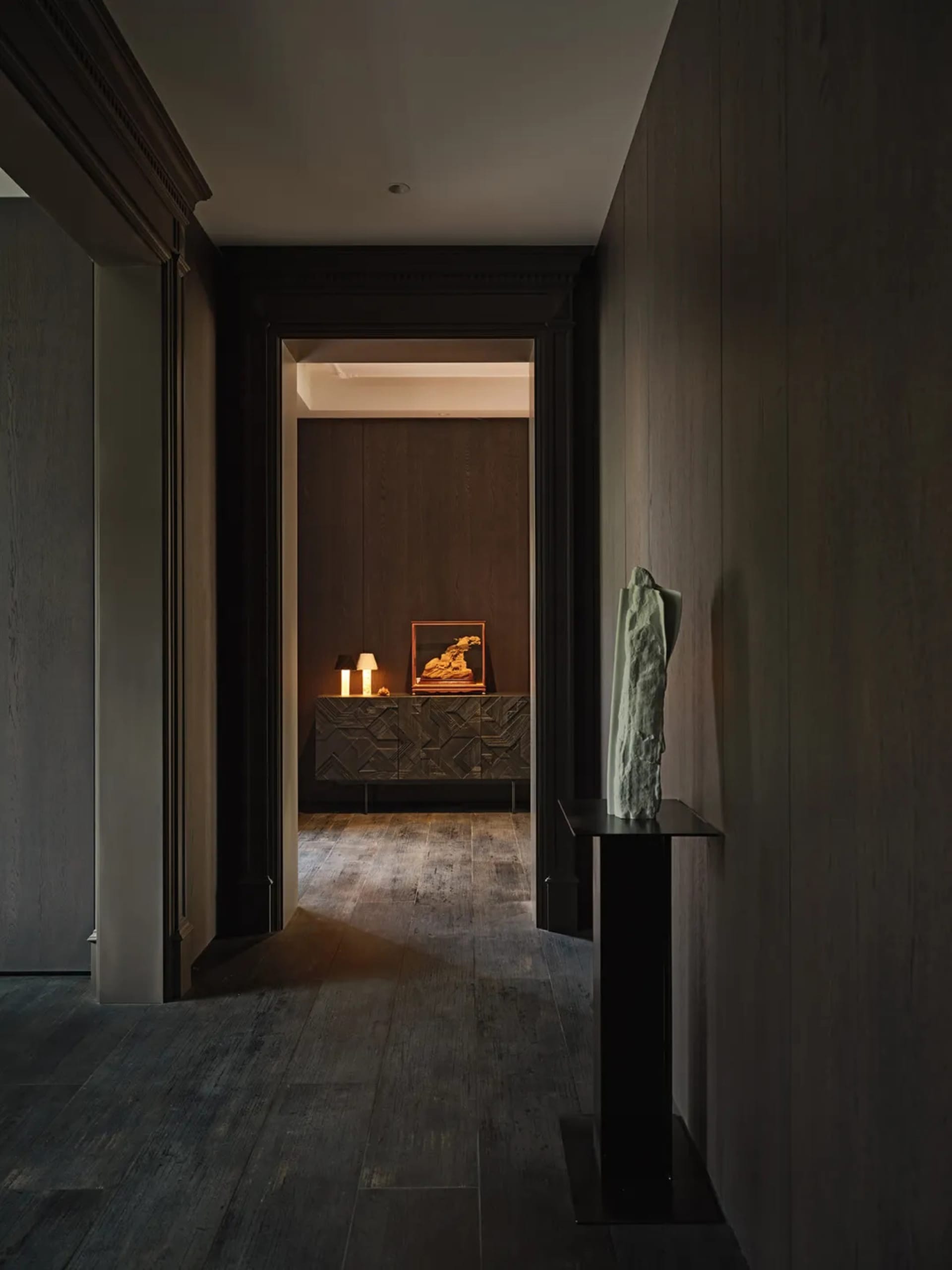 Interior design featuring a minimalist entrance with dark wood paneling, a table with a sculpture, and a sideboard with a pie