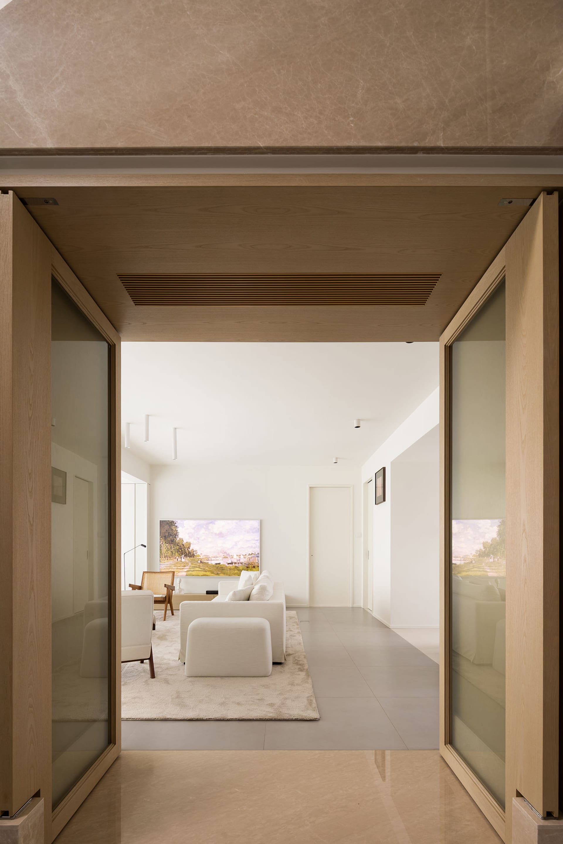 A modern living room with light brown material walls, white furniture, and a large artwork.