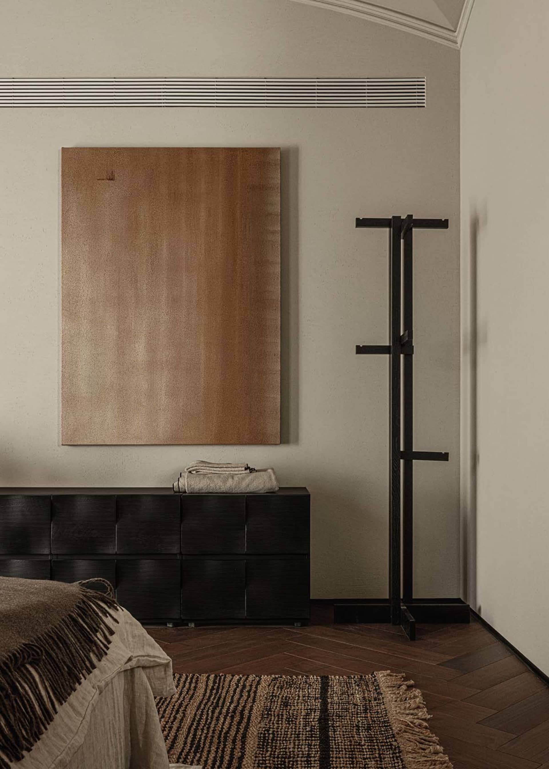 Modern minimalist bedroom with a black woven dresser, a beige and black rug, and a black metal coat hanger.