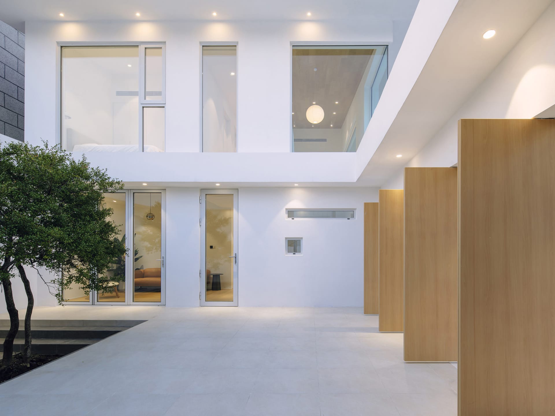 Modern minimalist interior with concrete and glass elements and a tree in a white courtyard.
