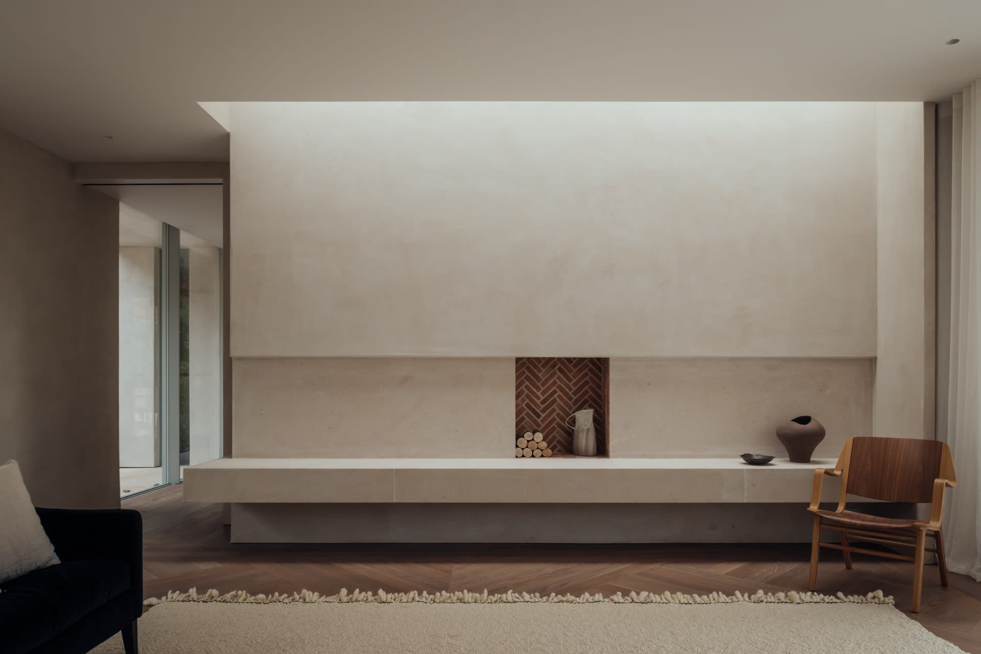 Modern minimalist living room with a concrete fireplace, wooden floor, and a few pieces of furniture.