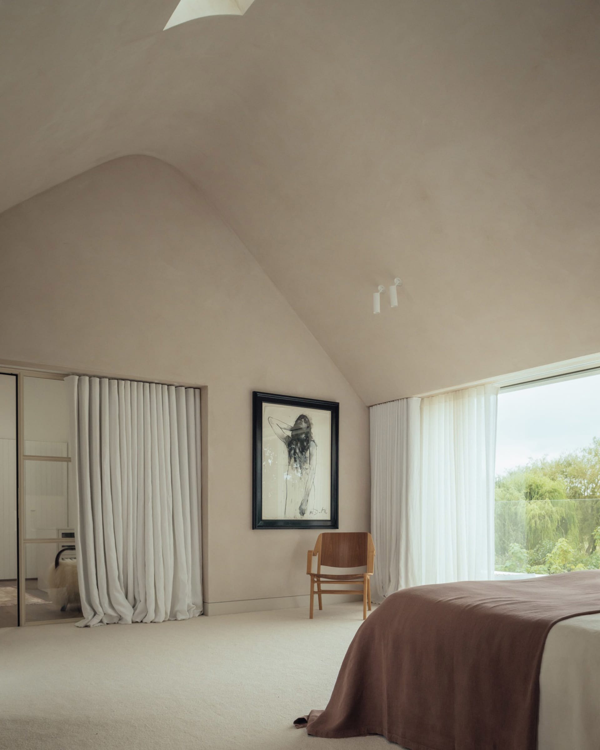 A minimalist bedroom featuring soft textiles, large windows, and a natural light-filled space.