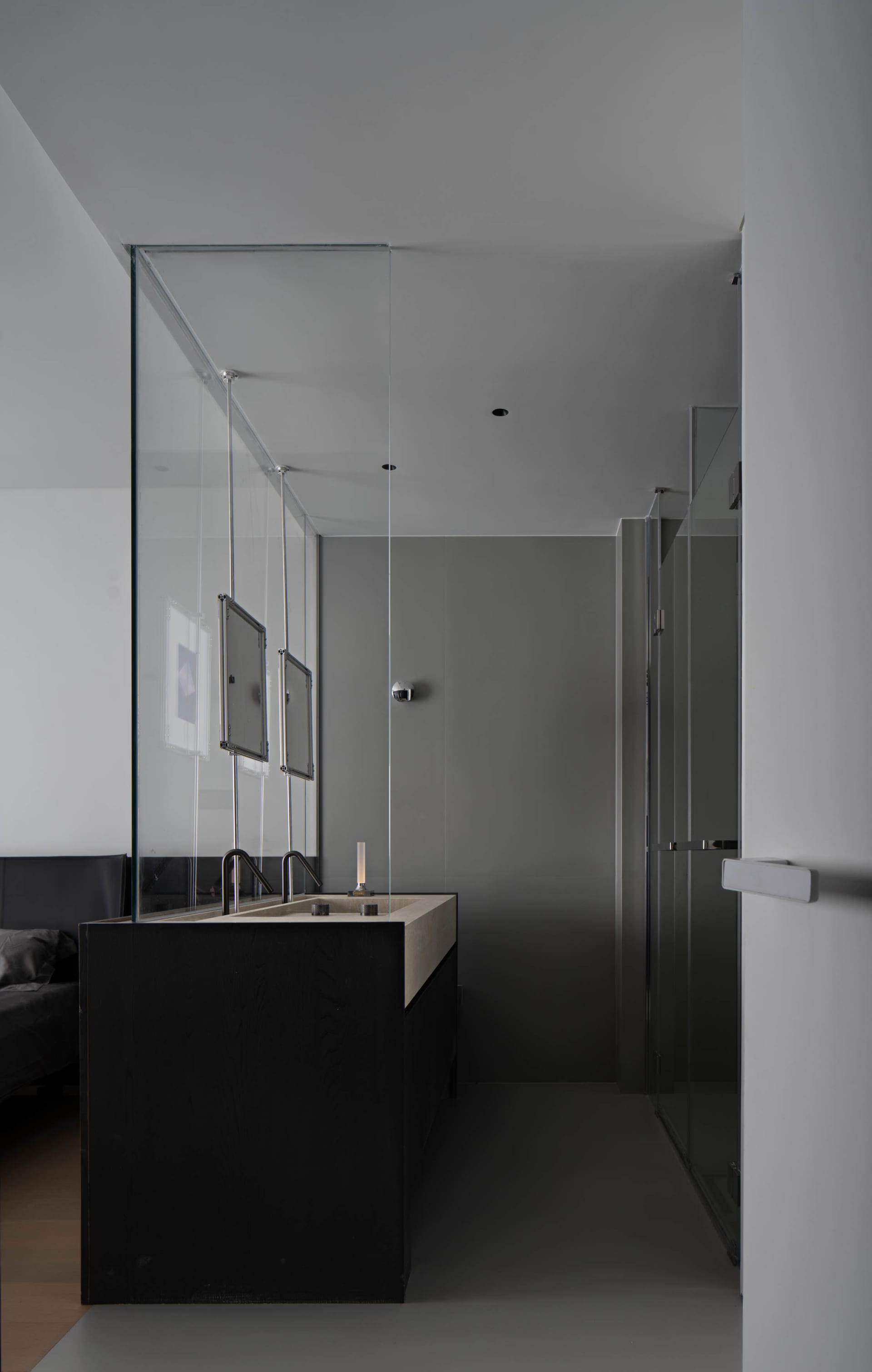A minimalist modern bathroom with concrete walls and floor, featuring sleek black cabinetry and a long sink counter.