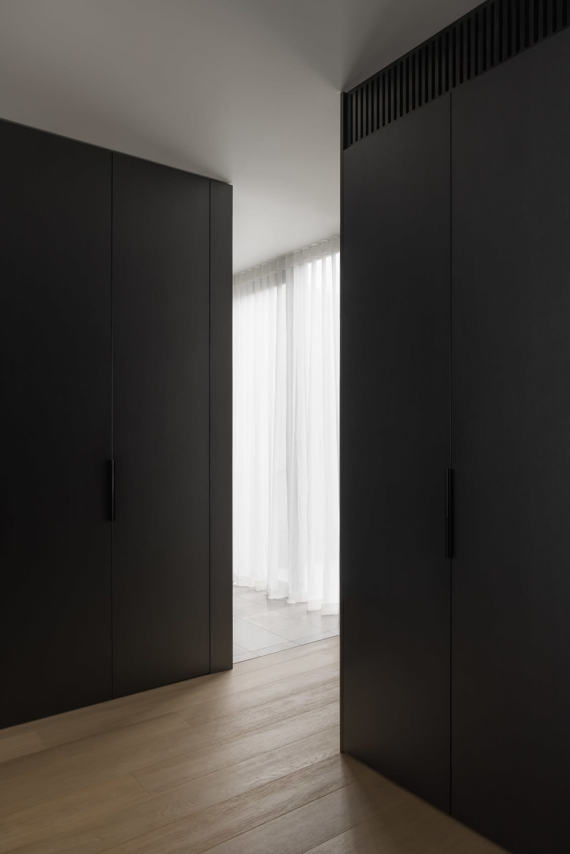A modern residential interior featuring dark wood flooring and black wardrobes.