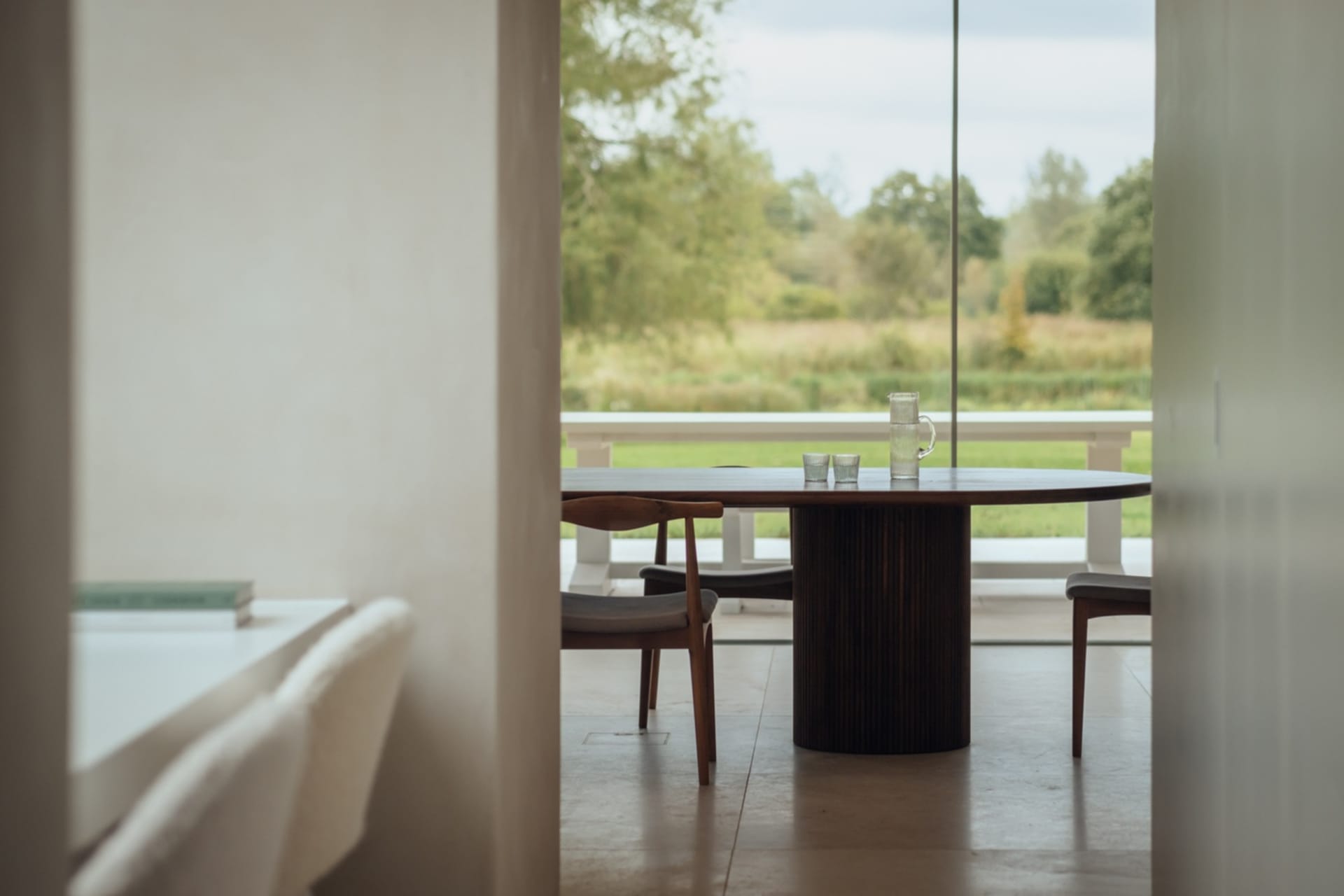 A modern interior space with a wooden table and chairs, featuring a large window overlooking a natural landscape.