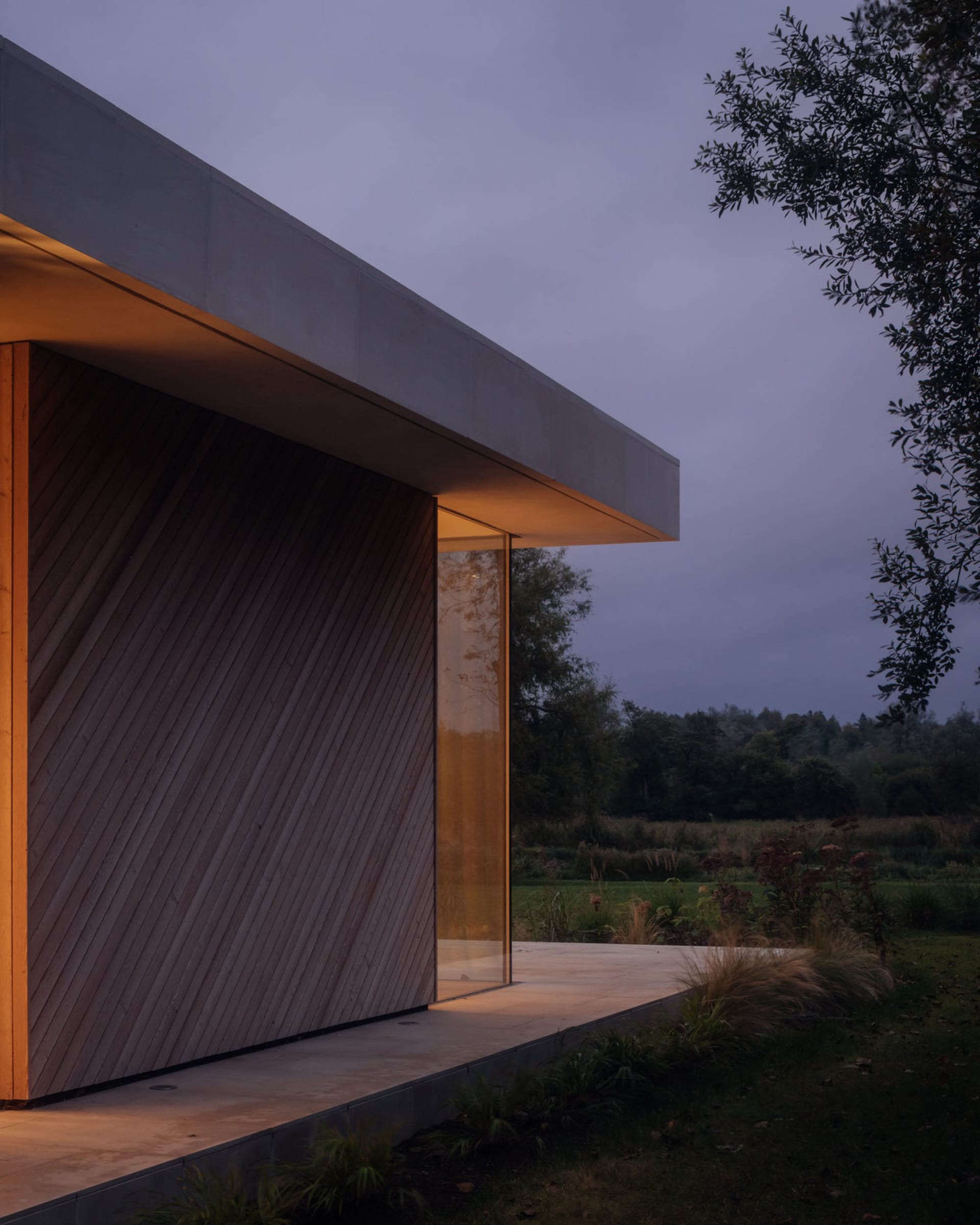 Modern residential exterior with wooden cladding and glass facade at dusk.