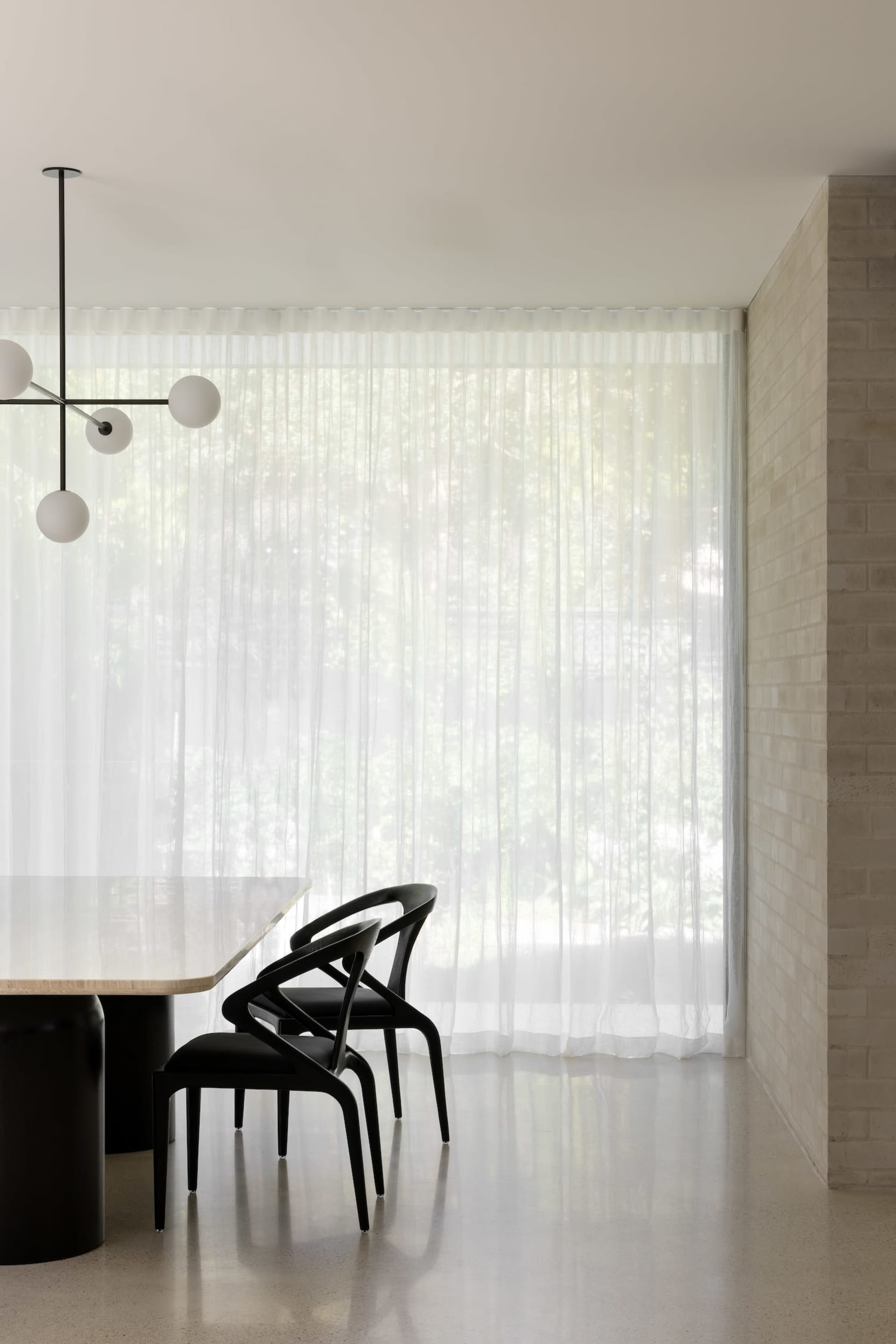 Minimalist modern dining room with concrete table and black chairs behind sheer curtains.