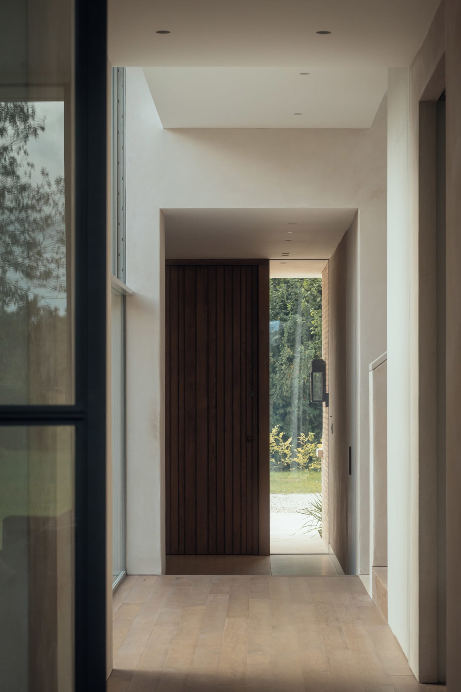 A modern entrance featuring a wooden door with a view of the garden.