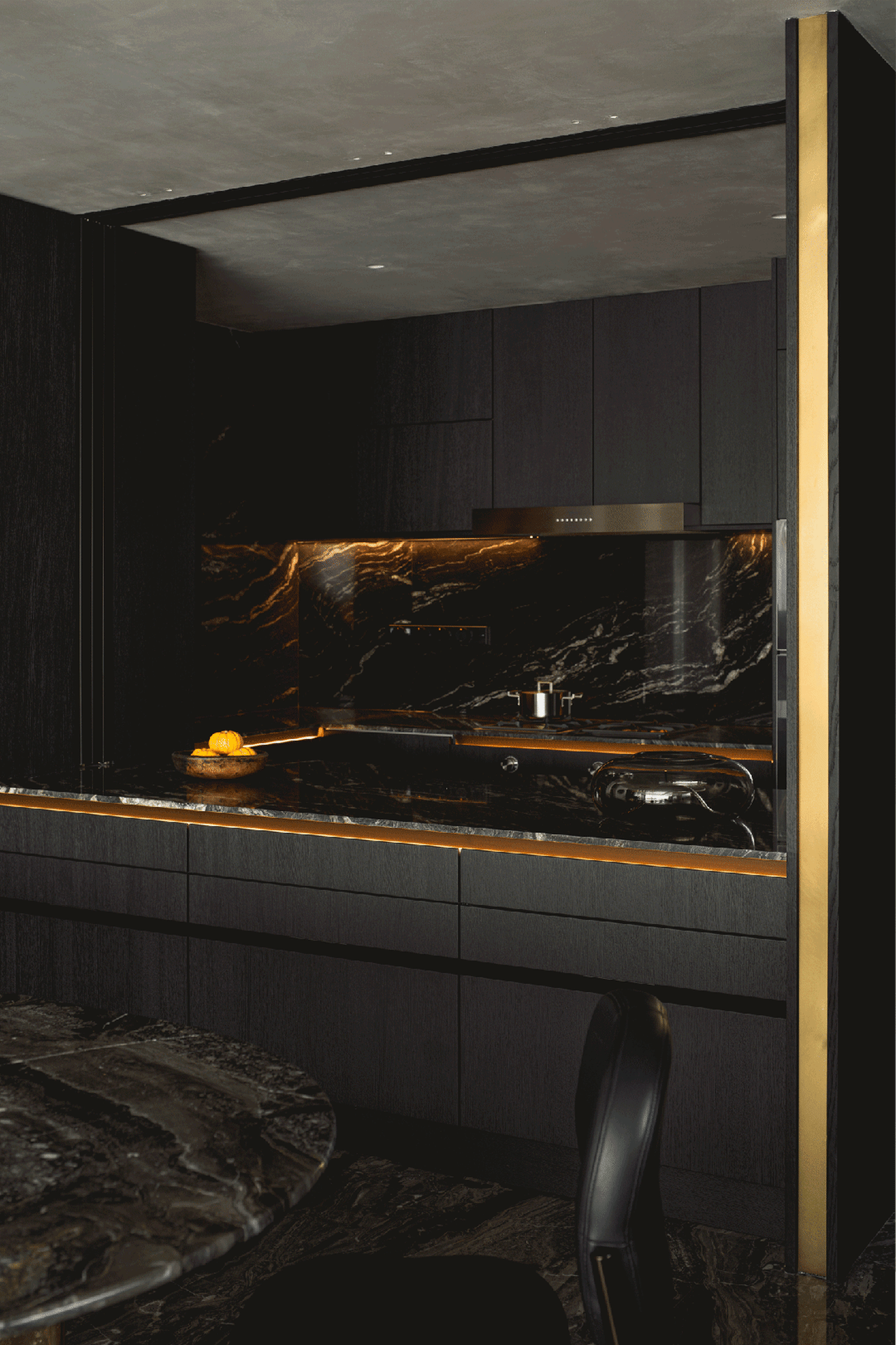 Modern kitchen with dark marble countertops, gold lighting, and black cabinetry.