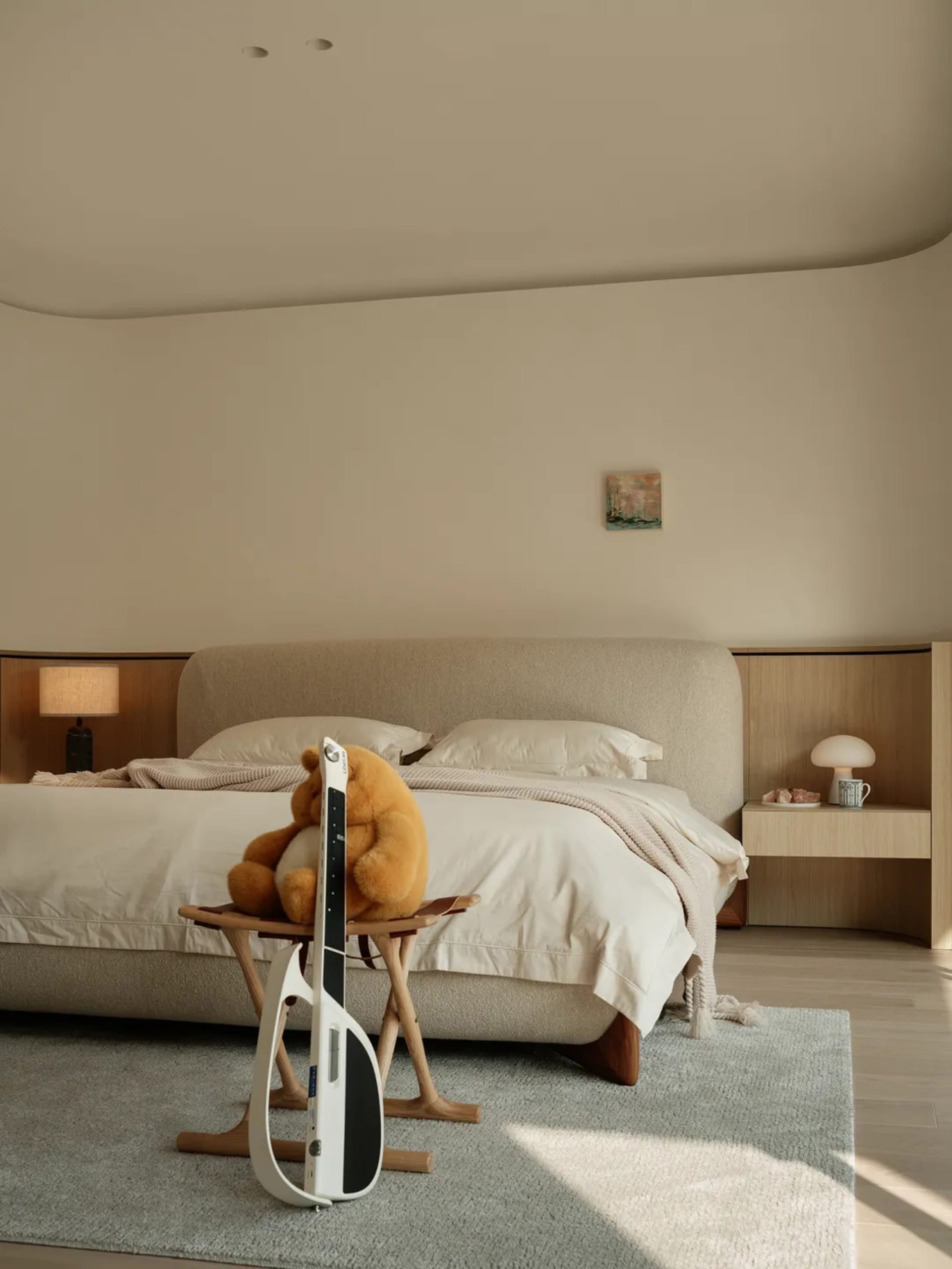 A minimalist bedroom with a beige upholstered bed, wooden nightstands, and a light blue rug.