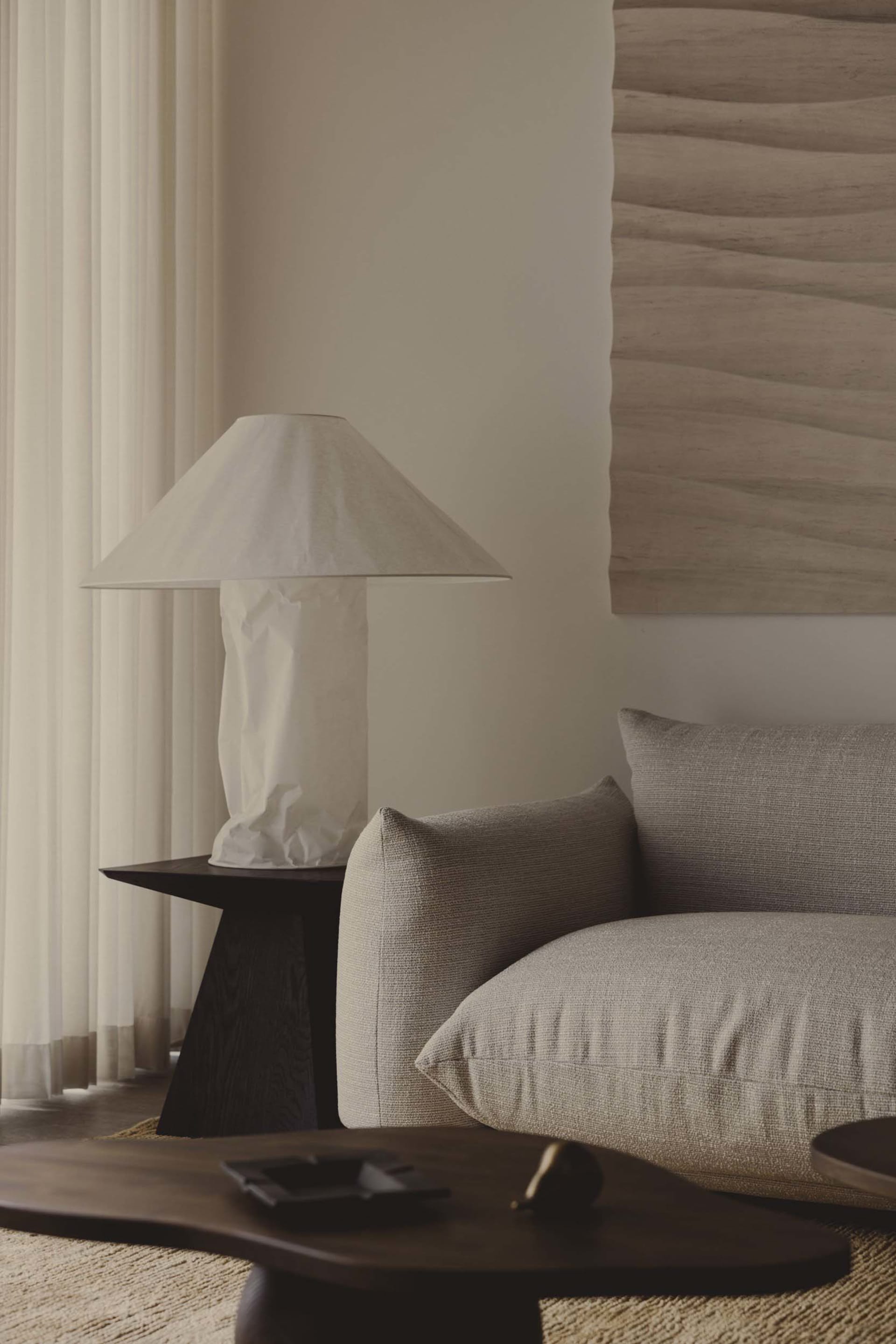 A minimalist living room with a neutral-toned fabric sofa, wooden coffee table, and patterned fabric pillows, all situated in