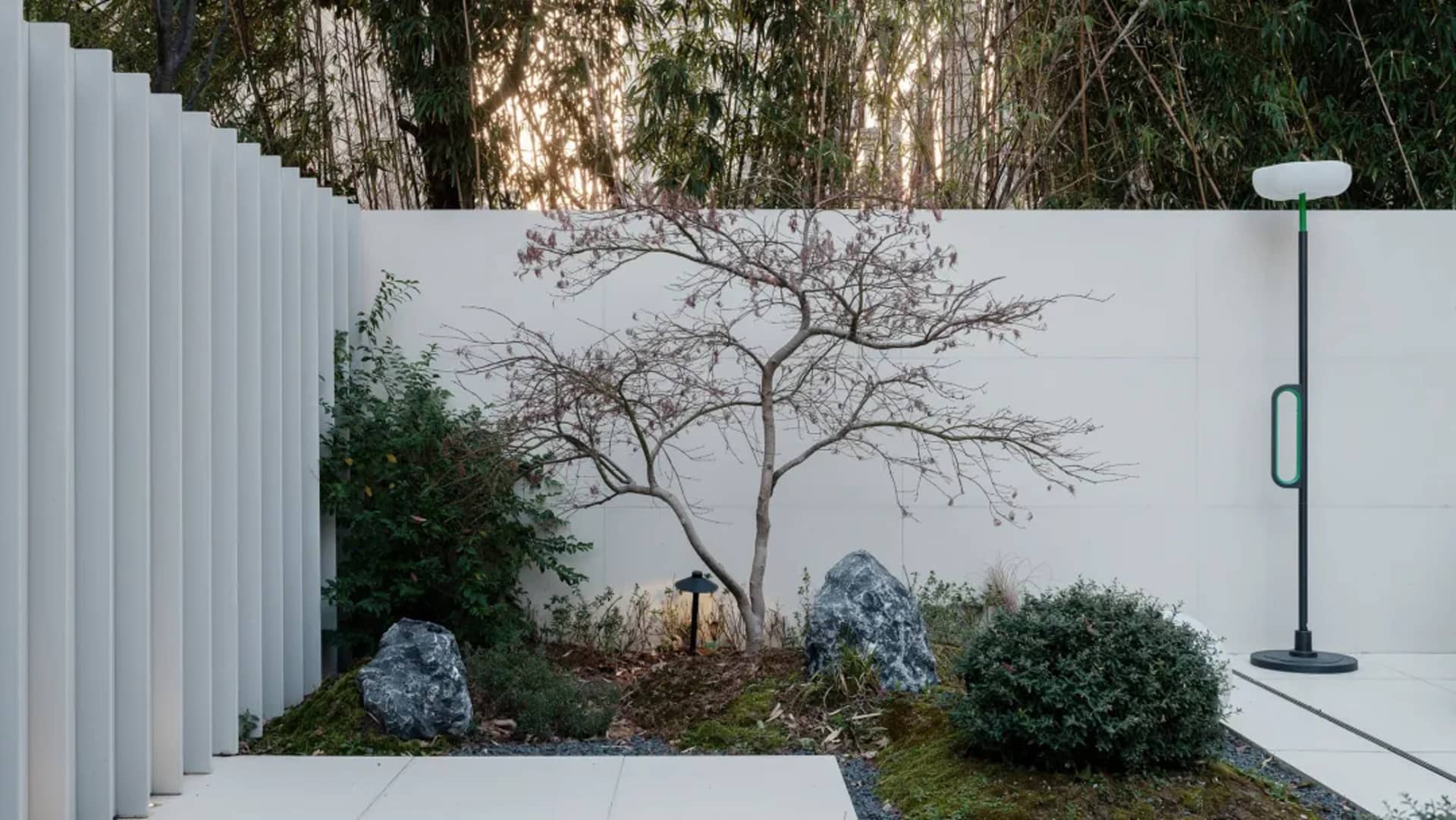 現代極簡後院，採用混凝土、樹木、岩石與綠植，搭配白色牆面及綠白燈具