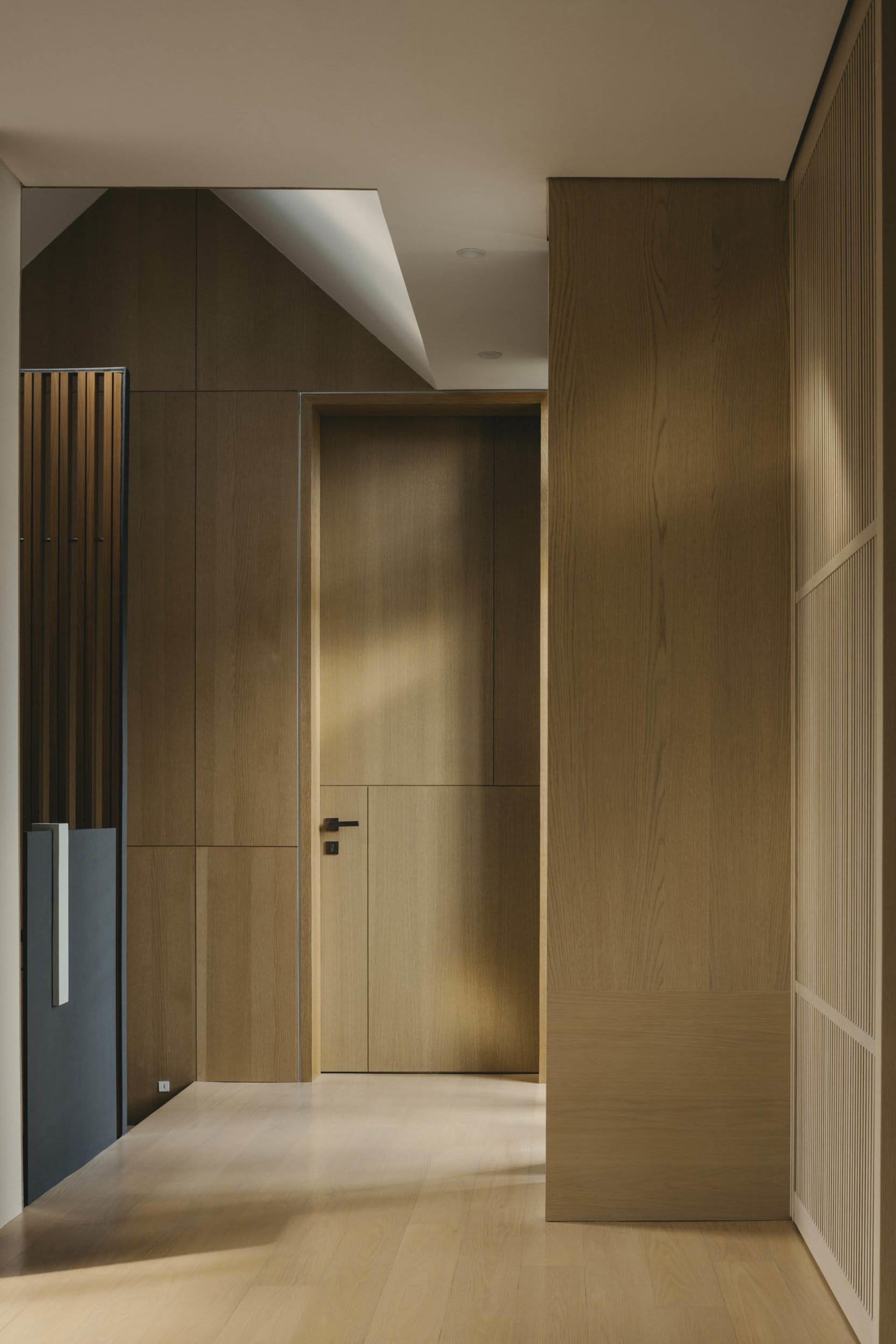 A modern interior designed with wooden paneling, featuring a door and a ceiling light.