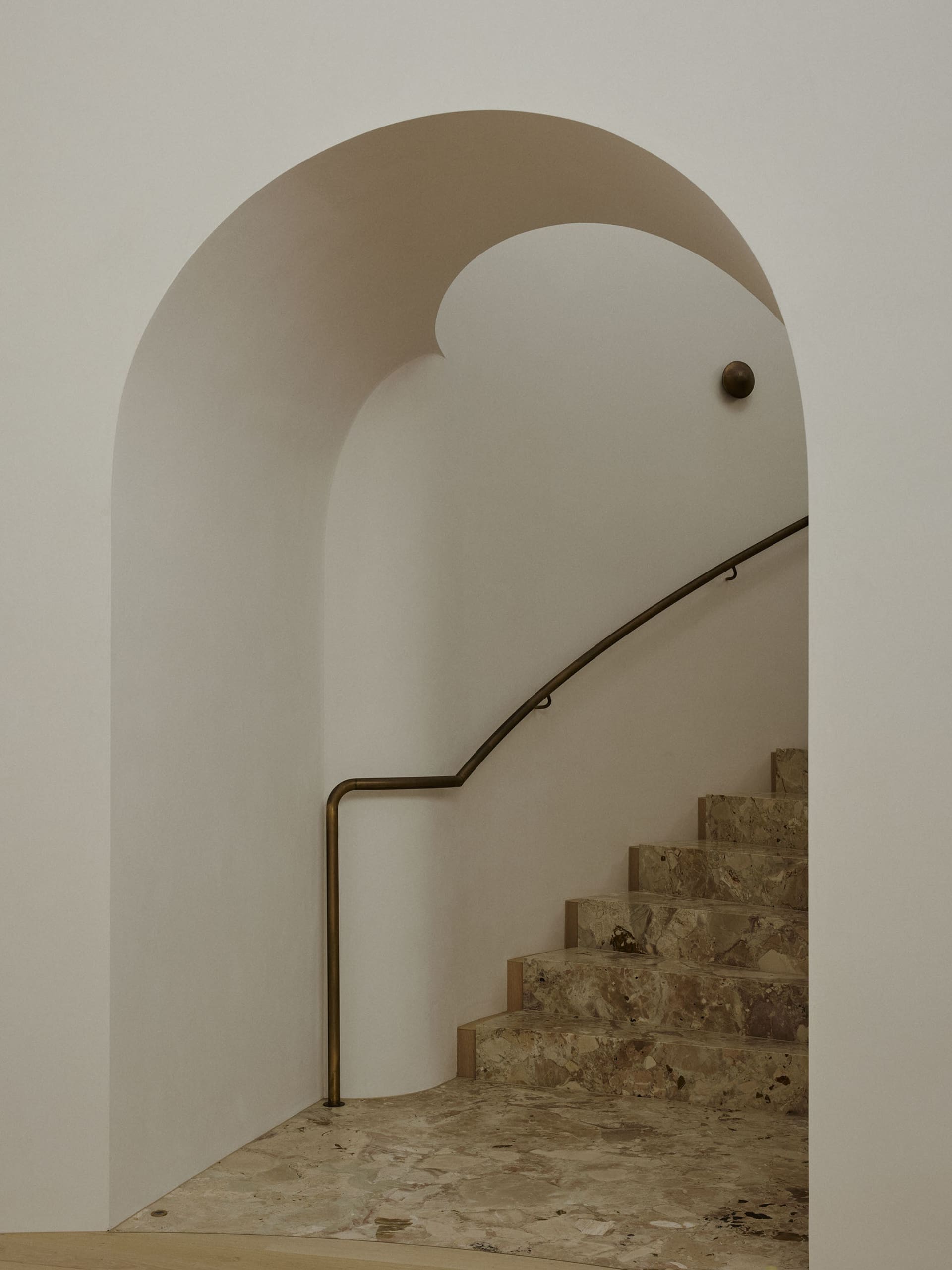 A modern marble staircase with curved walls and a bronze handrail.