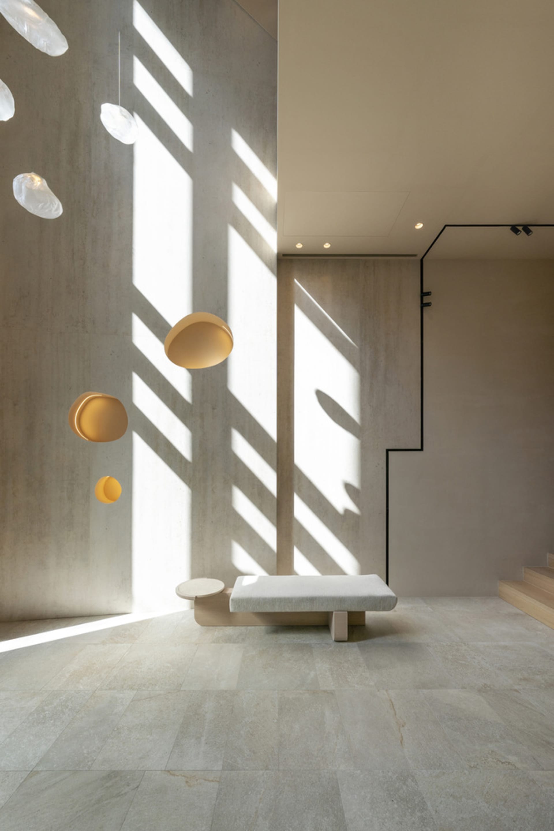 A minimalist interior space featuring exposed concrete walls, a white bench, and floating circular lights.