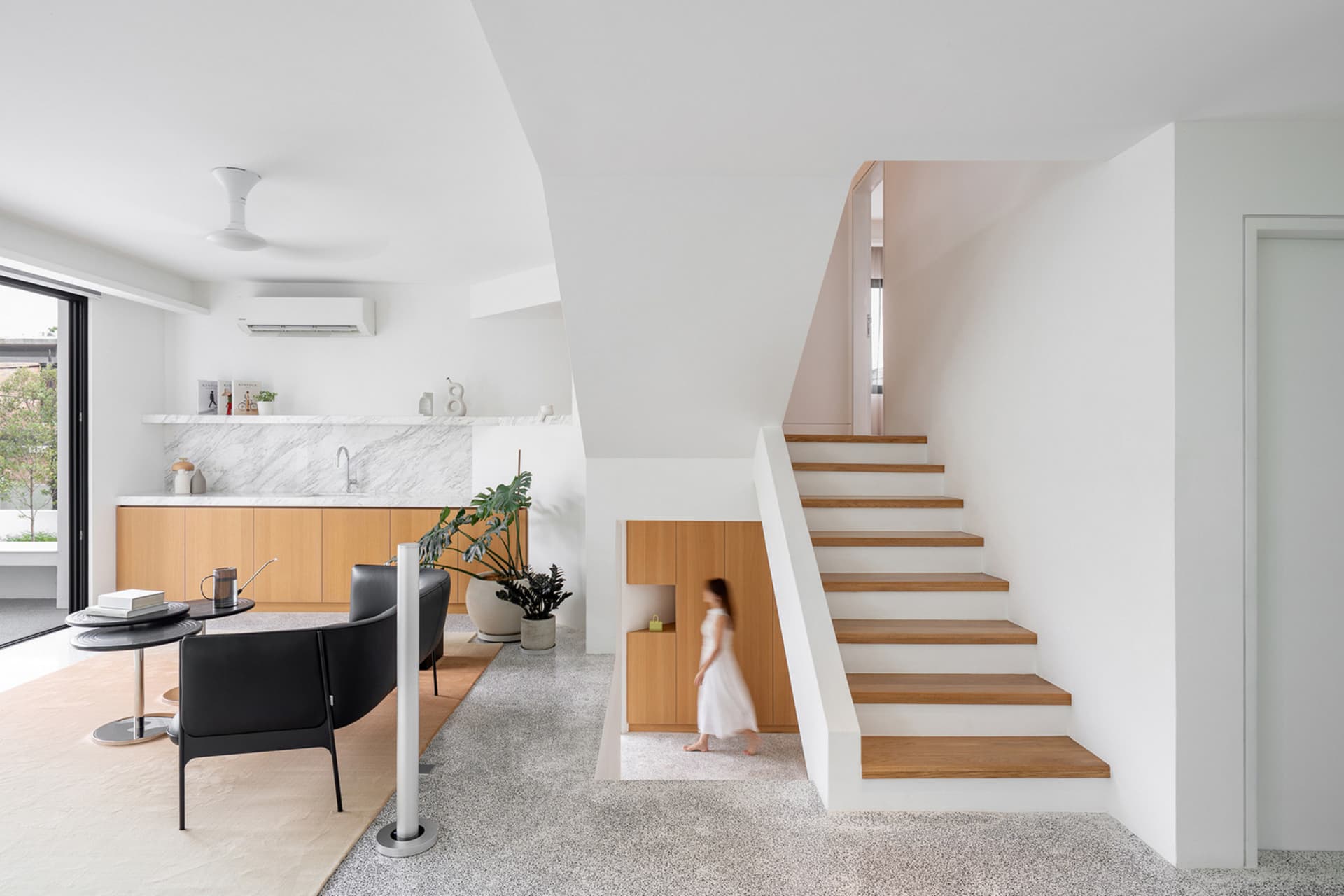 A modern residential interior featuring a staircase with white marble and wooden steps, white walls, and wooden cabinetry.