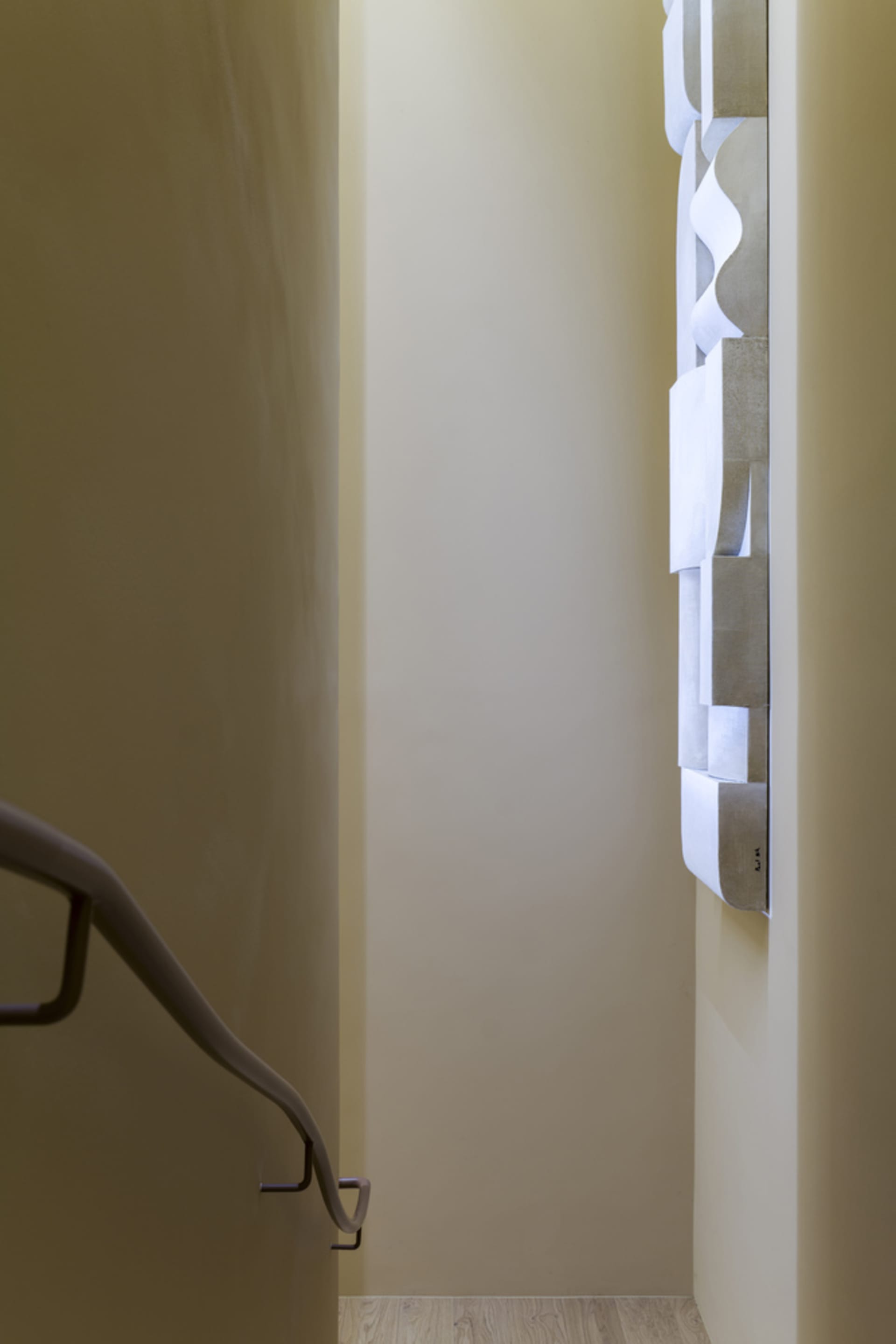 A vertical metal railing enhances the modern design of a stairwell, adorned with a unique wall showcasing white sheets of pap