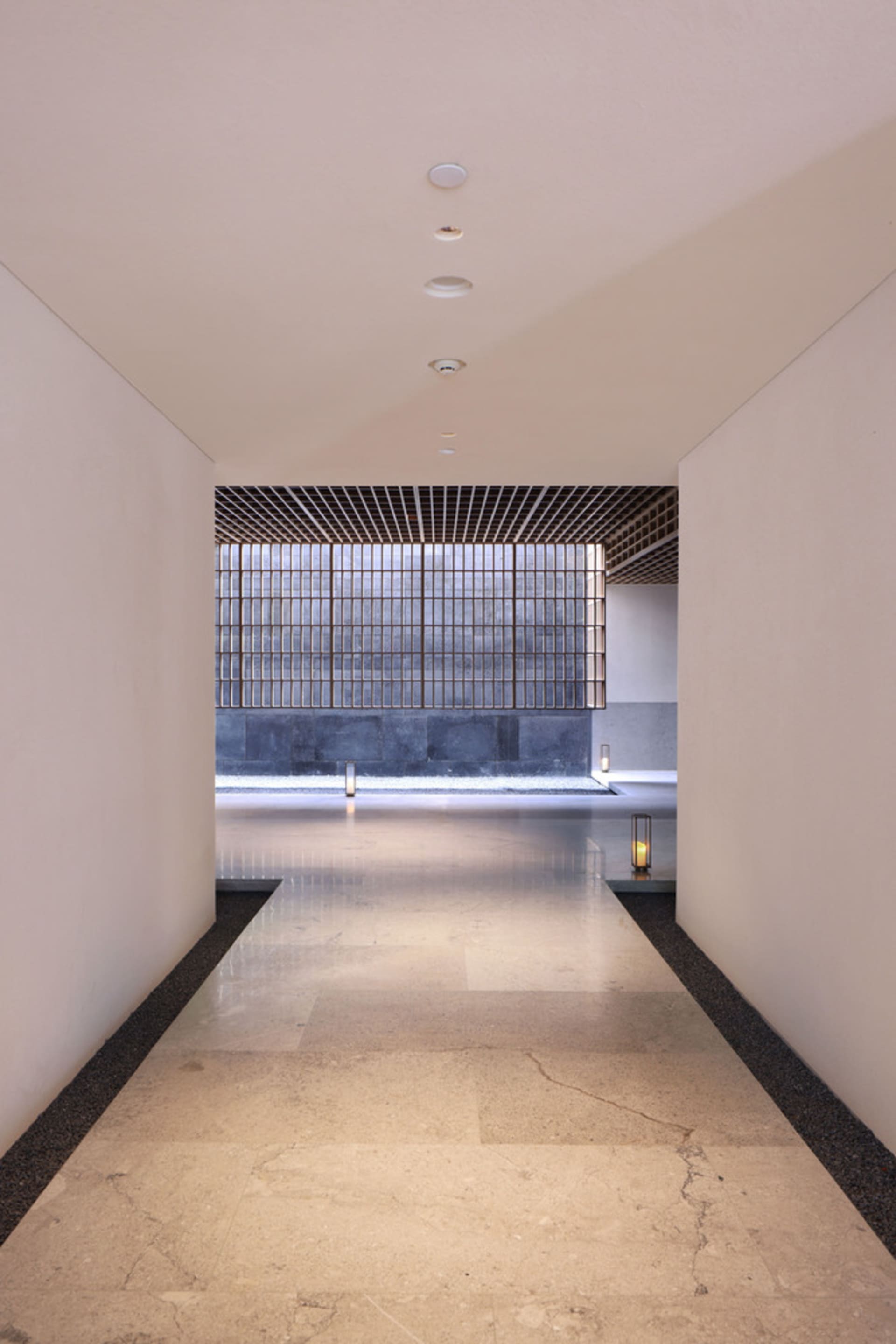 Long, spacious entrance hall with smooth marble tiles, leading to a black-framed glass wall.