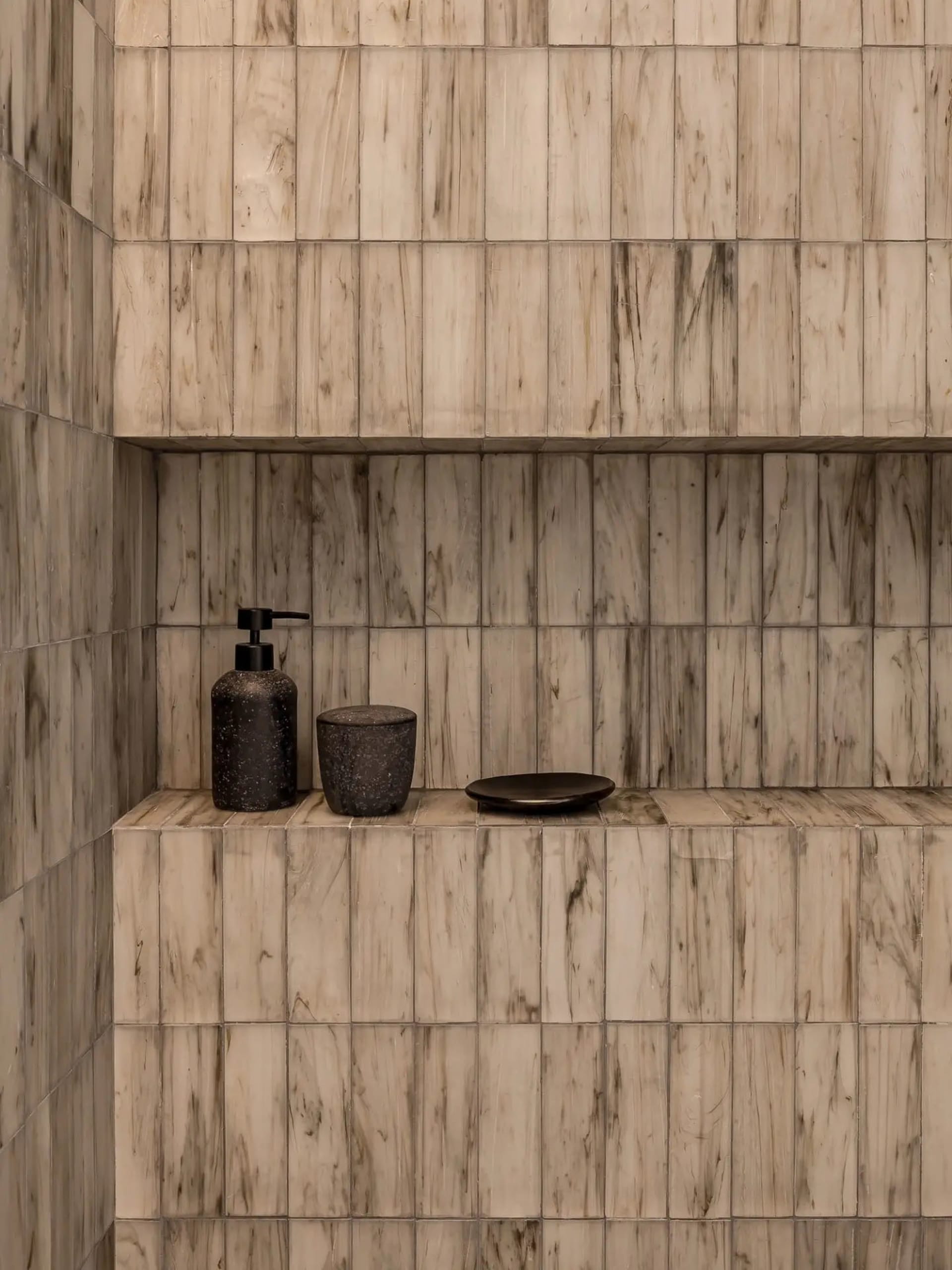Modern bathroom featuring marble tiles with integrated storage shelves and small black items.