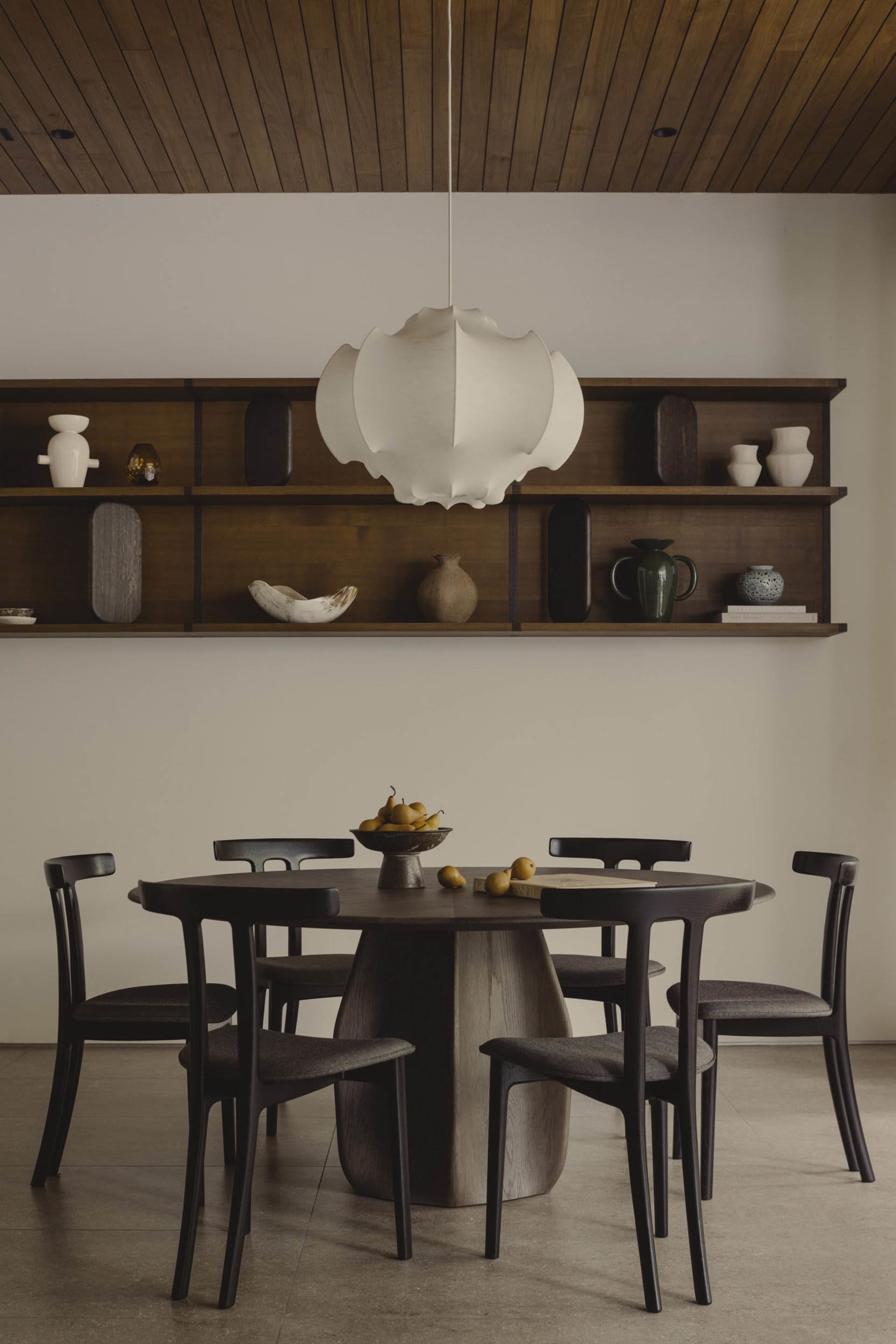 Modern dining room with wooden furniture, pendant light fixture, and wall-mounted shelves.