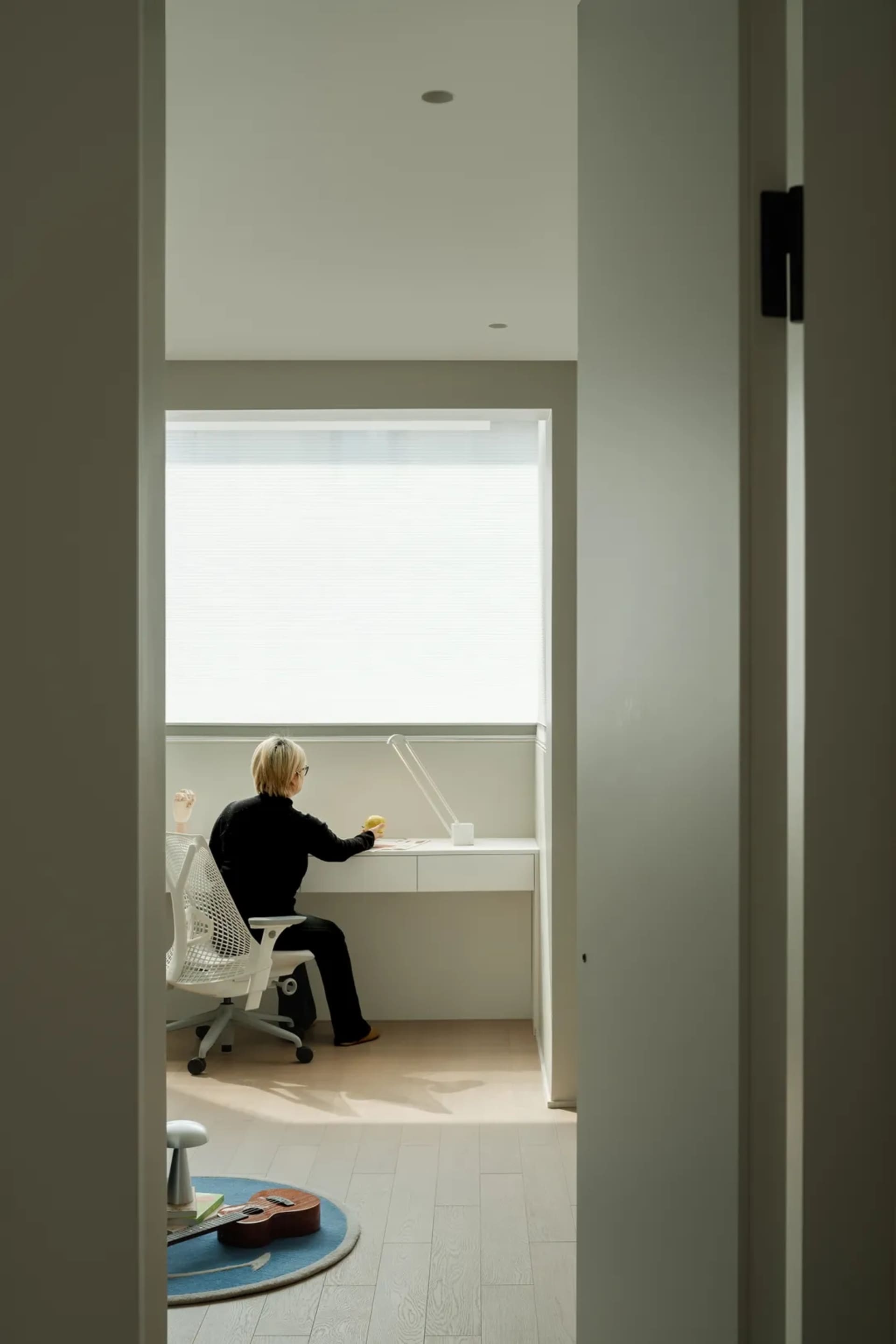 A modern home office desk setup with a person sitting at it, illuminated by a lamp.