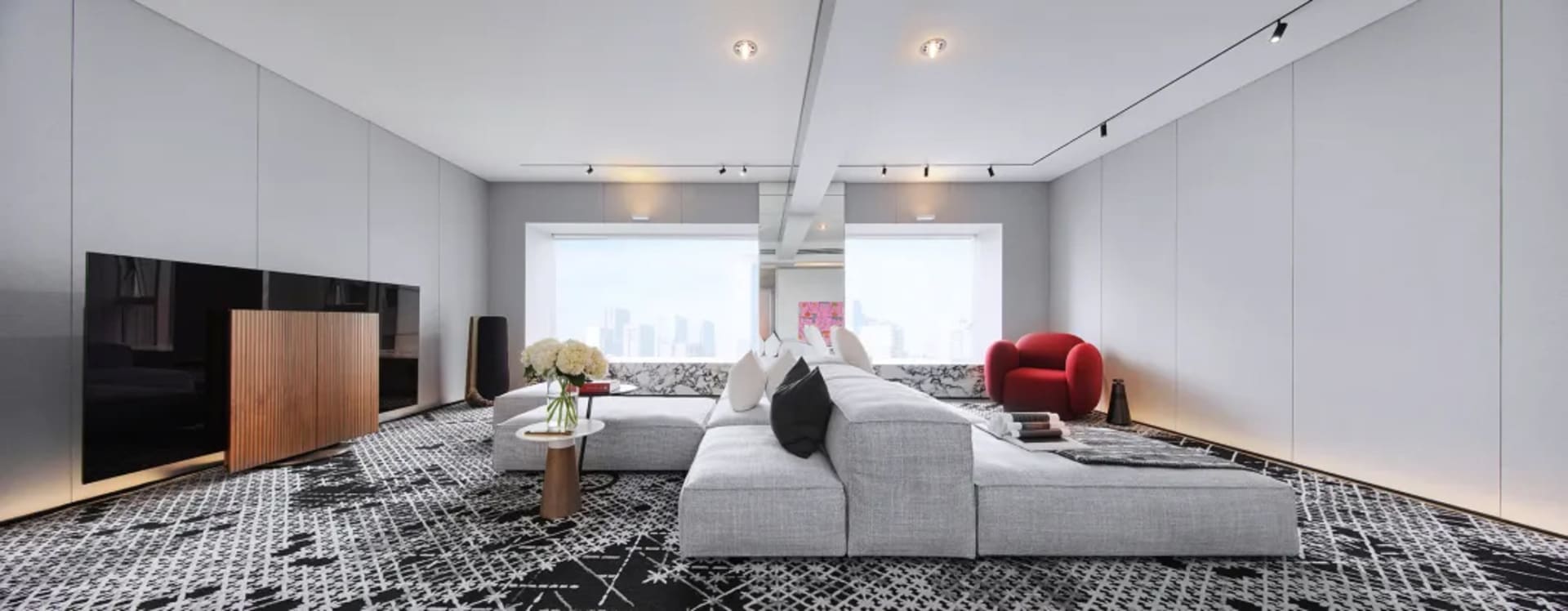 Modern living room with grey sofa, black and white patterned rug, large windows, and cityscape view.