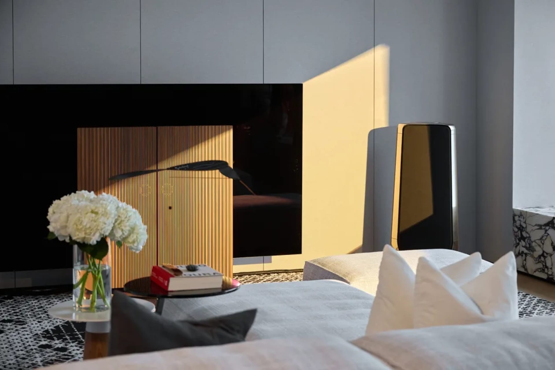 A modern living room with wooden accents, featuring a wooden cabinet, white cushions, and a vase of white flowers.