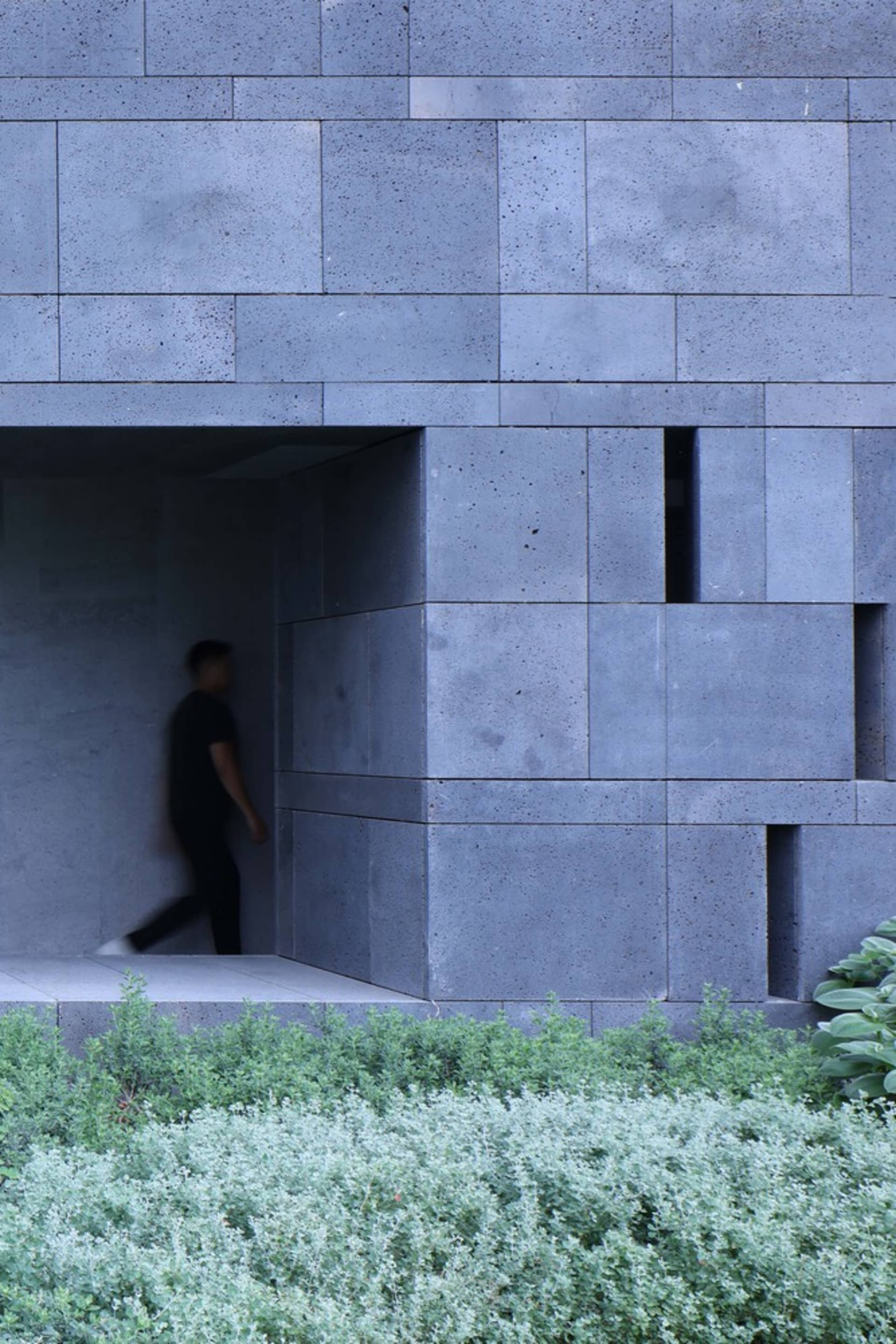 A modern minimalist concrete facade with a person walking in the background.