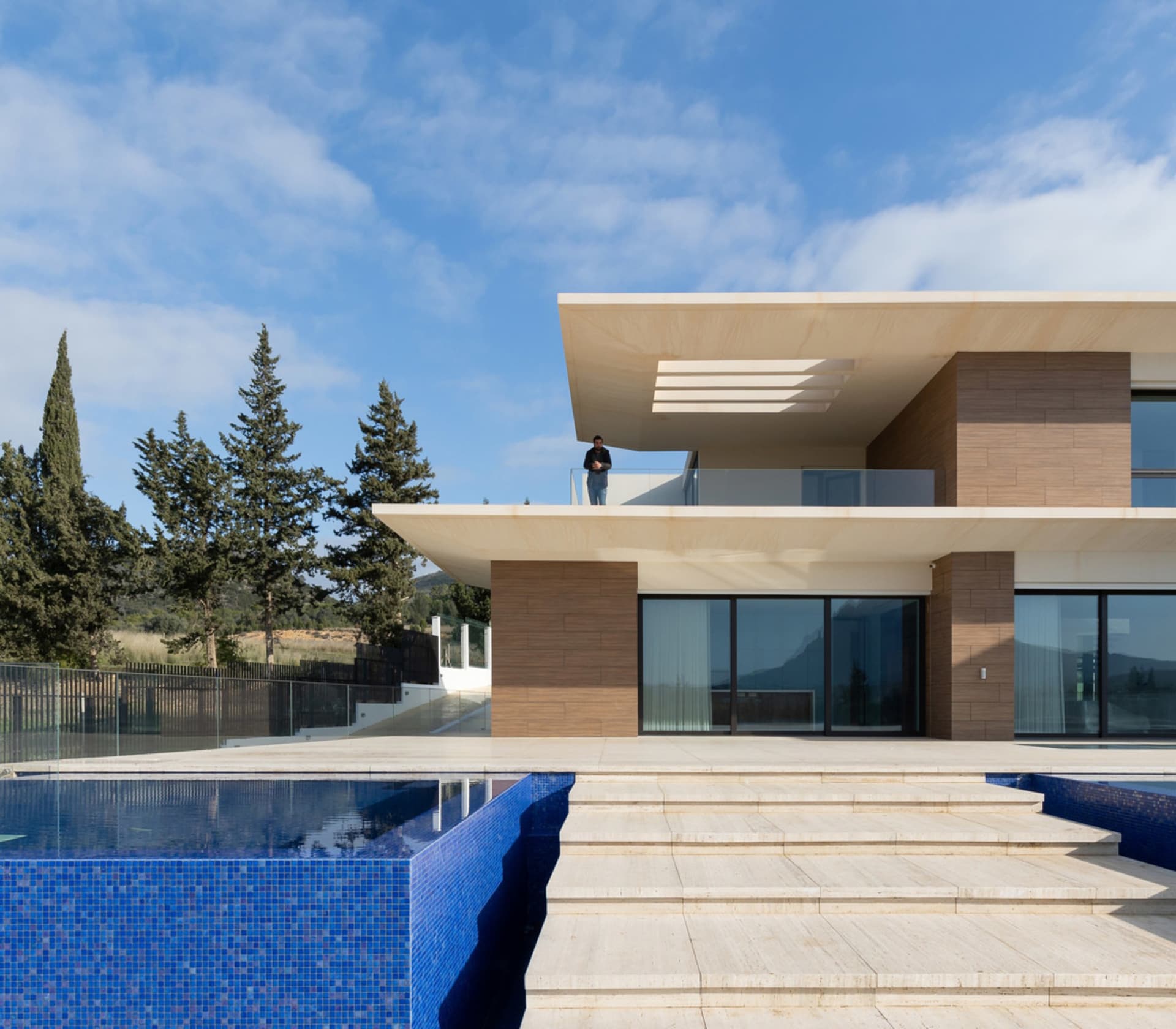 A modern residential exterior featuring glass, wood, and stone materials.