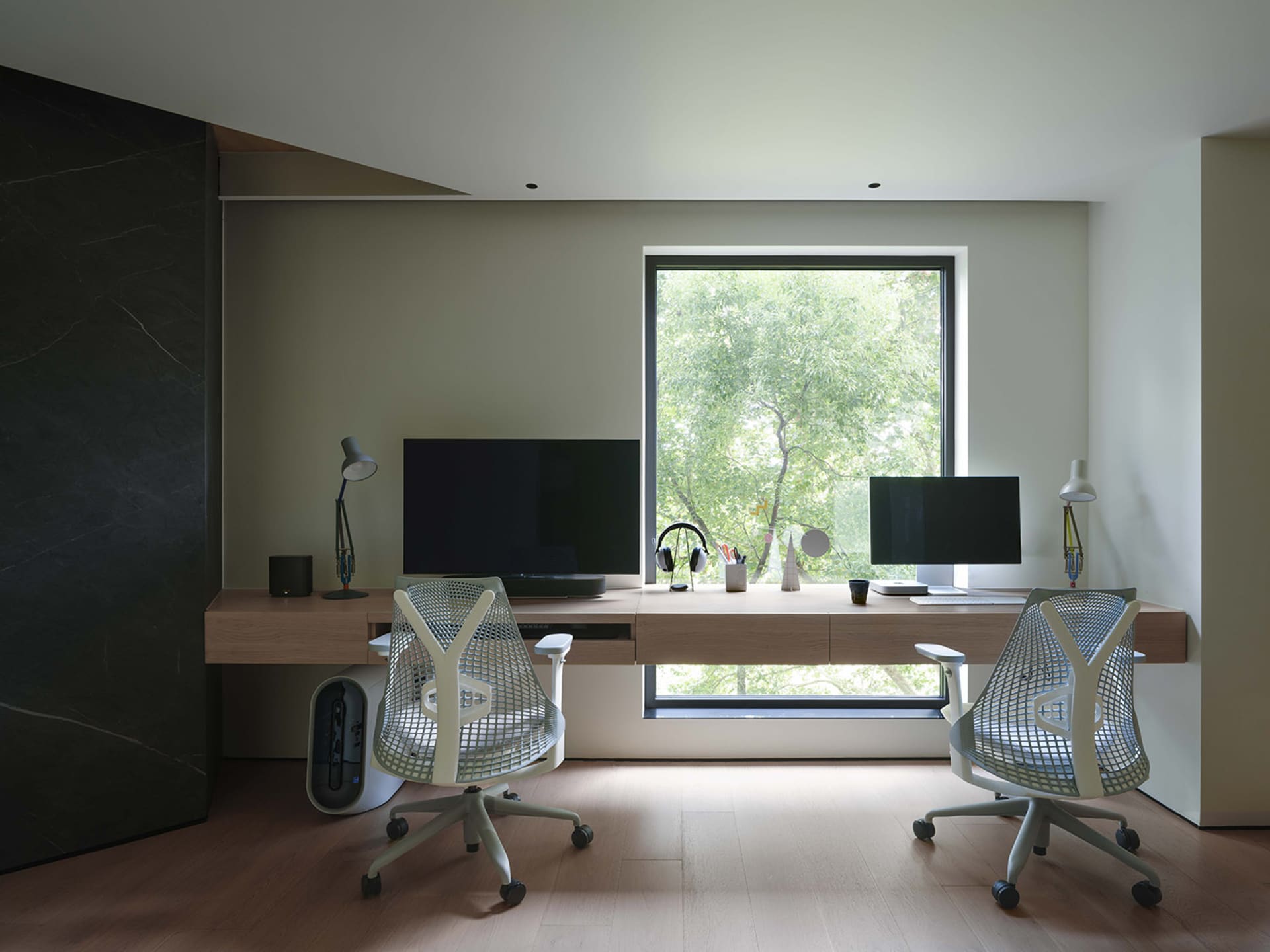 A modern minimalist workspace with a wooden desk and chairs, featuring two computers and a large window.