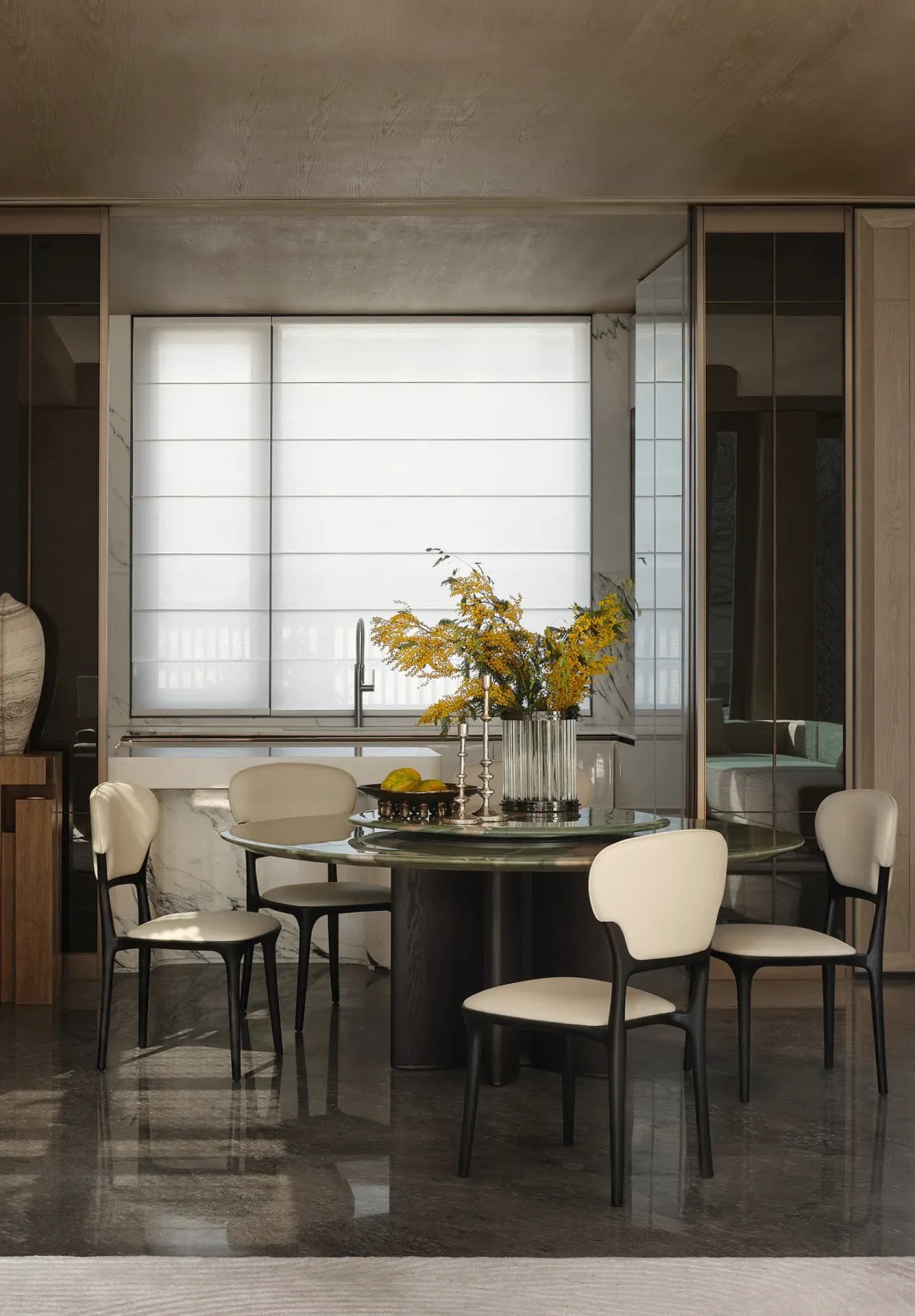 Modern dining room featuring a marble table and chairs, with a vase of yellow flowers and a bowl of fruit in the center of th
