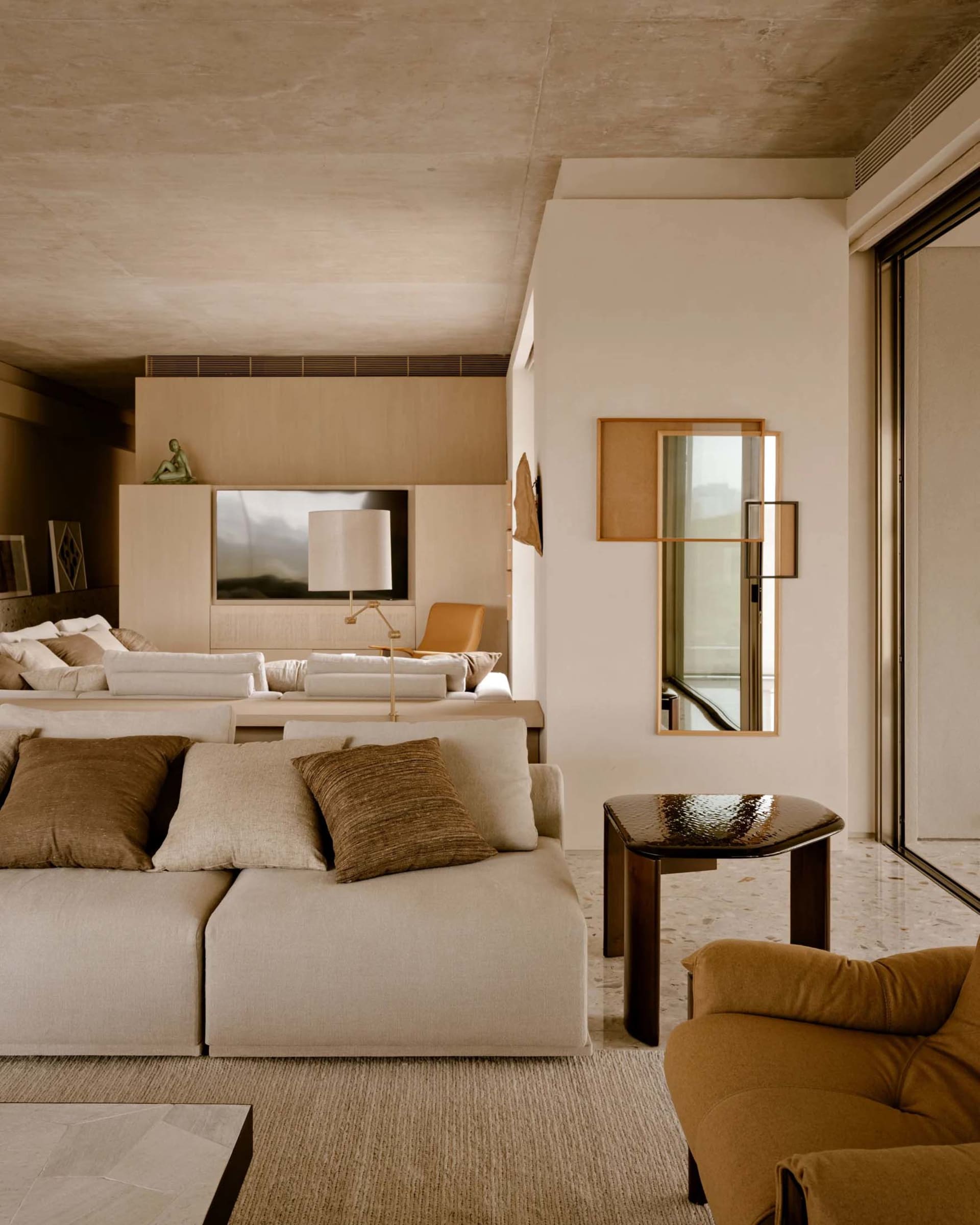 A minimalist living room featuring concrete walls and furniture with earthy tones and textures.
