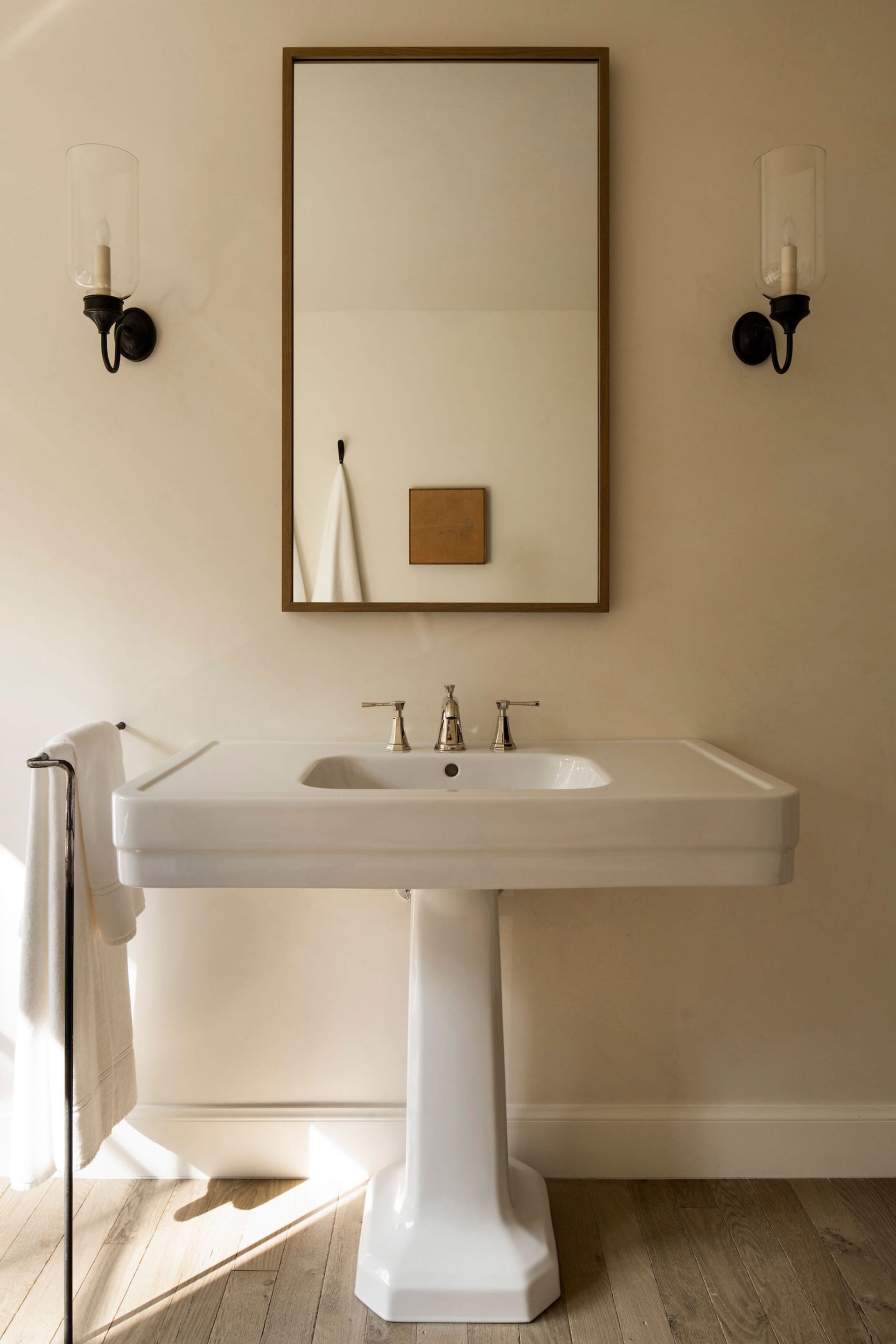 Modern bathroom featuring a ceramic sink with a pedestal base, two faucets, and a framed mirror above, with sconces on either