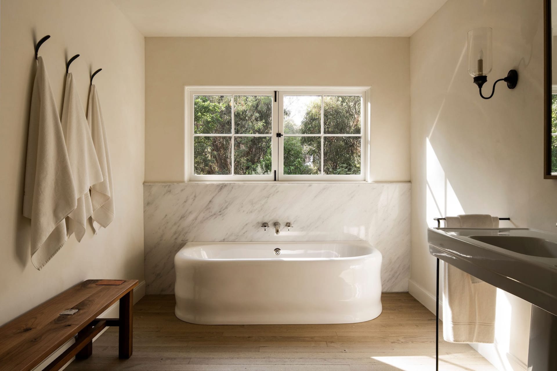 Modern bathroom designed with marble and ceramic materials, featuring a freestanding bathtub, towel hooks, and a sink with a 