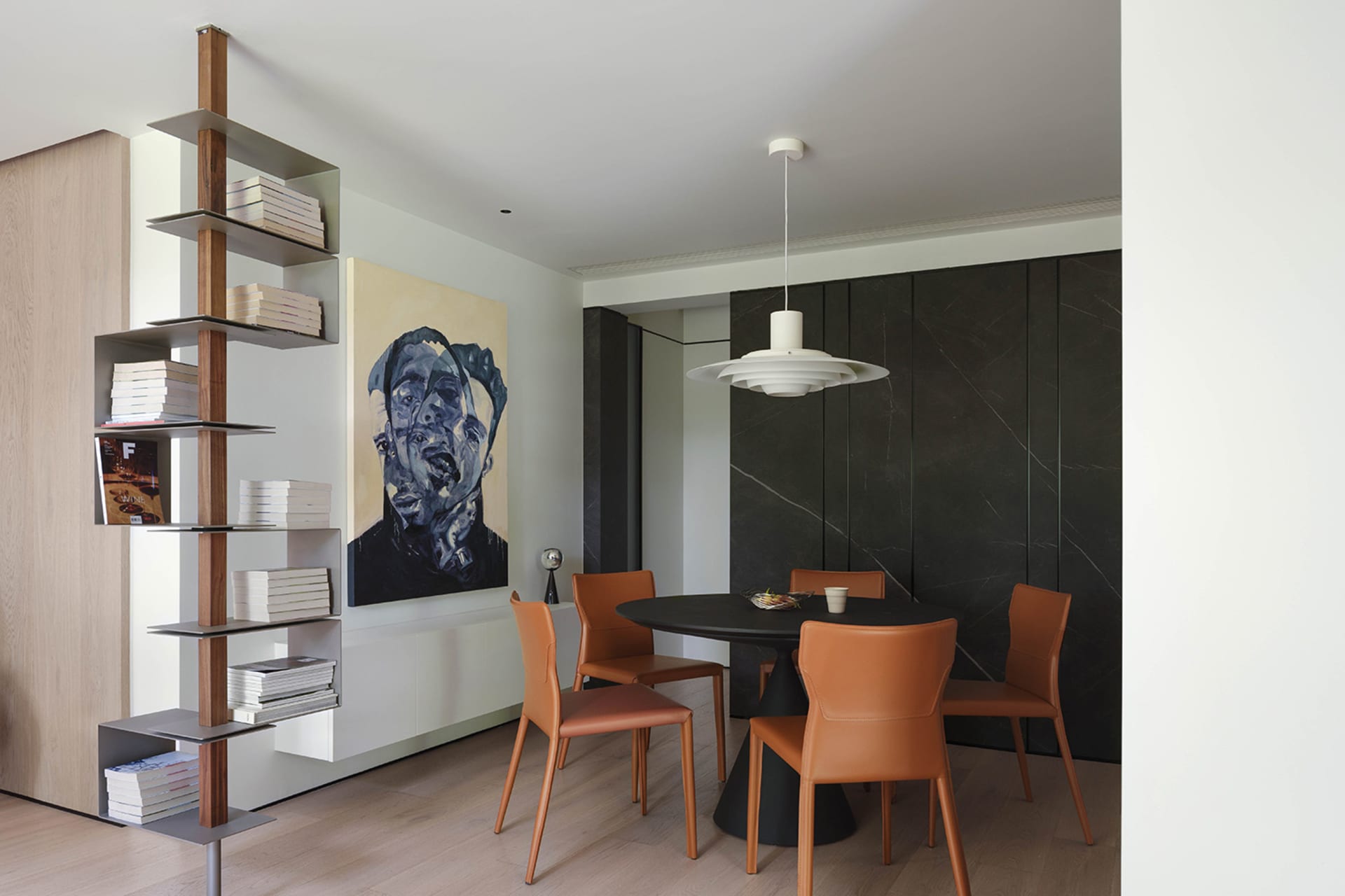 Modern dining room featuring a round black table surrounded by four orange chairs, a bookshelf filled with books, and a large