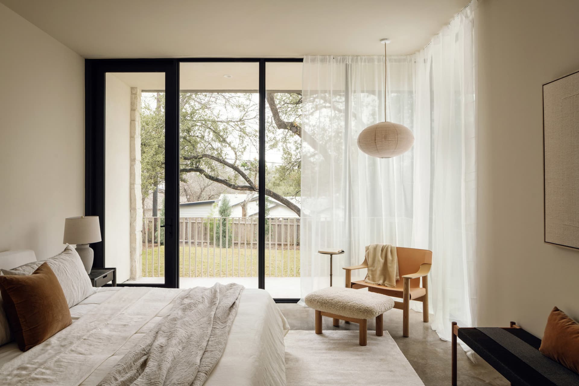 A minimalist bedroom with natural fibers, featuring a bed, side table, armchair, and footstool.