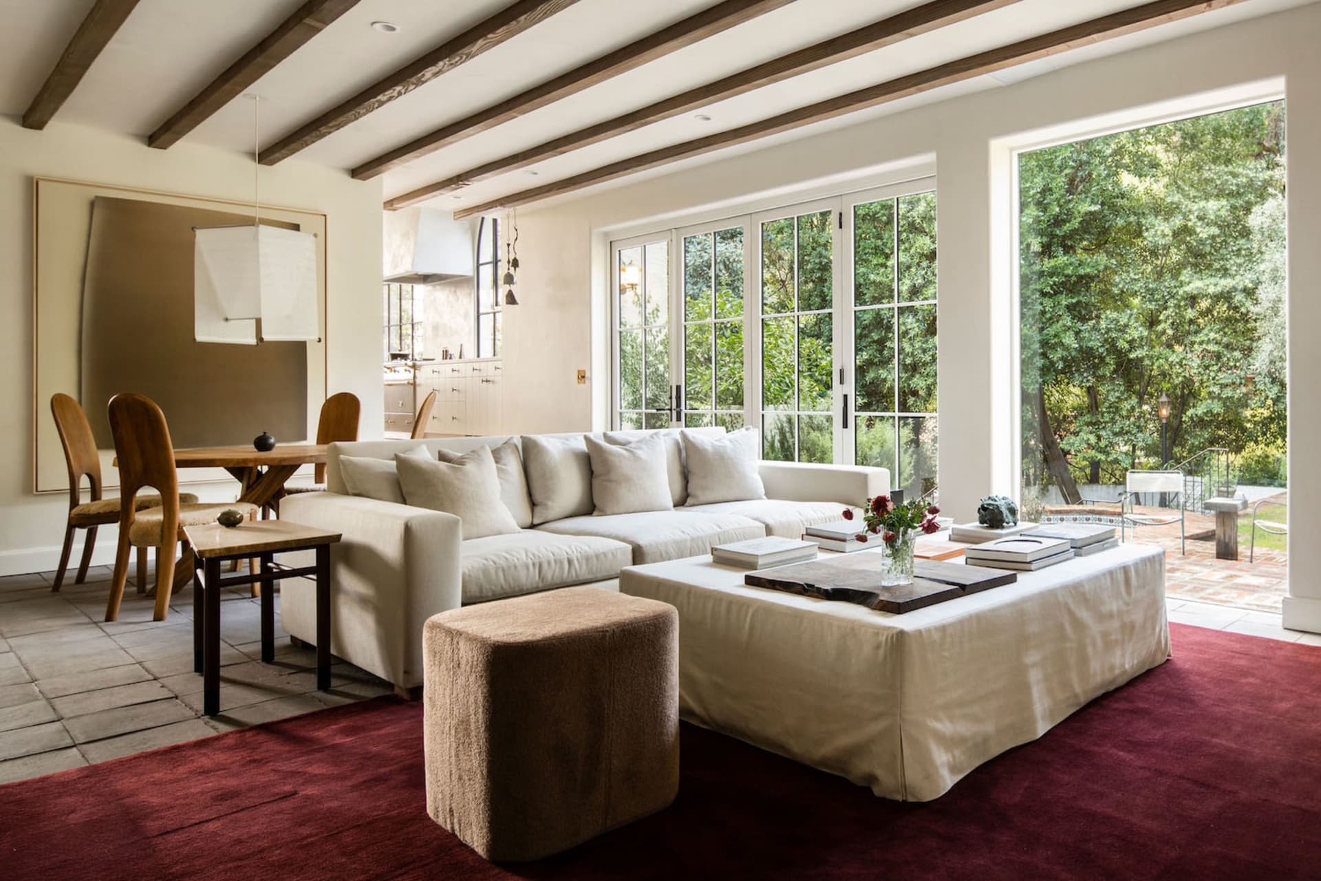 Modern living room with a white sectional sofa, wood floors, and large windows overlooking greenery.