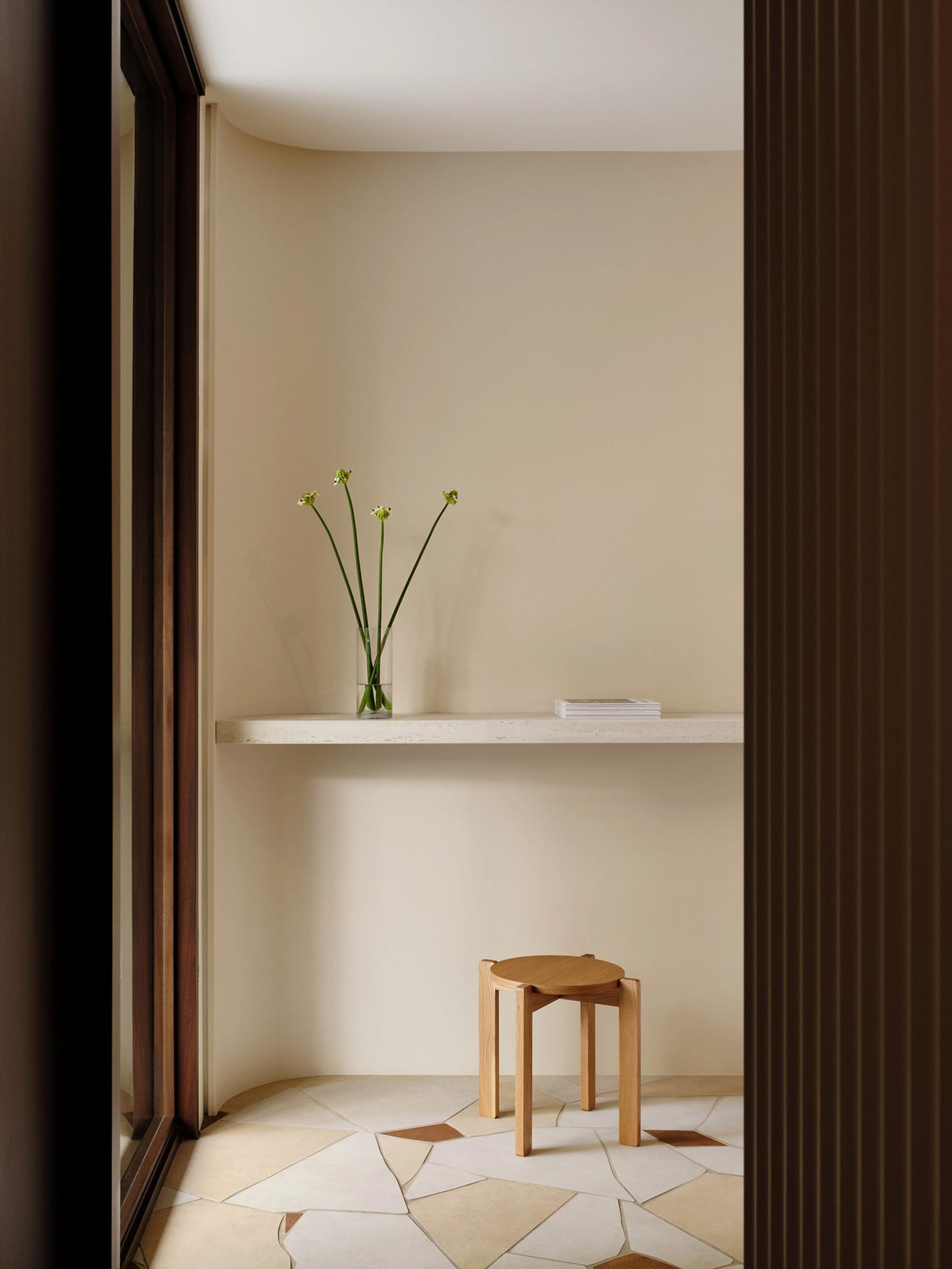 A minimalist interior design featuring a terrazzo floor with organic shapes and a concrete floating shelf holding a vase of g