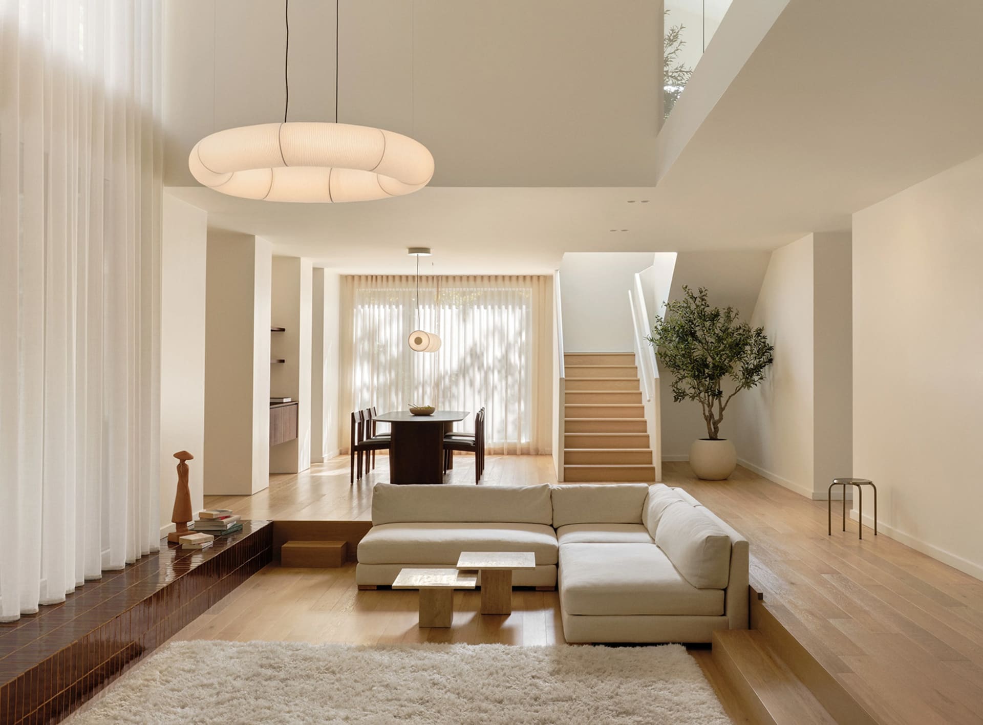 A minimalist living room with wooden elements, featuring a sectional sofa and a white rug.
