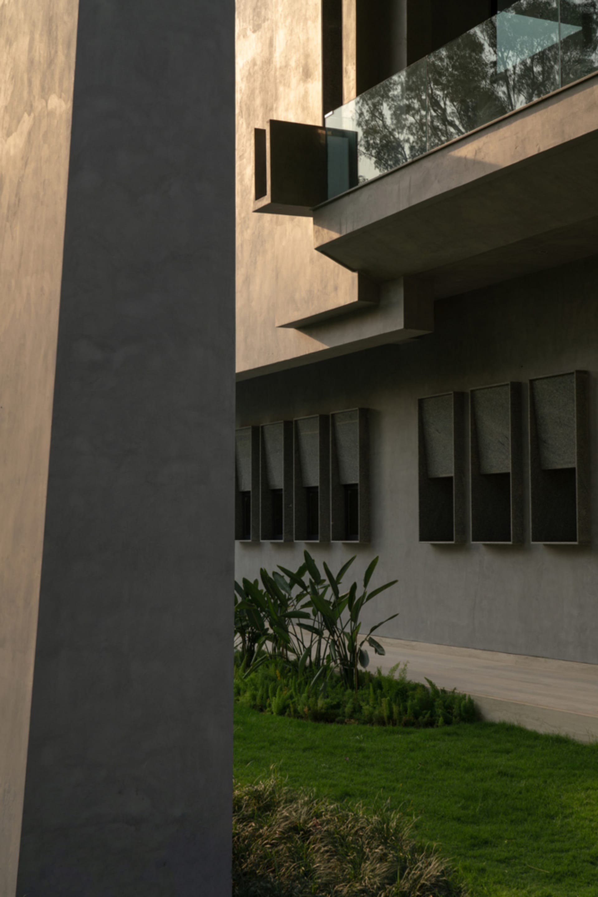 Modern, sleek, concrete building exterior with large glass window panels and green plants in foreground.