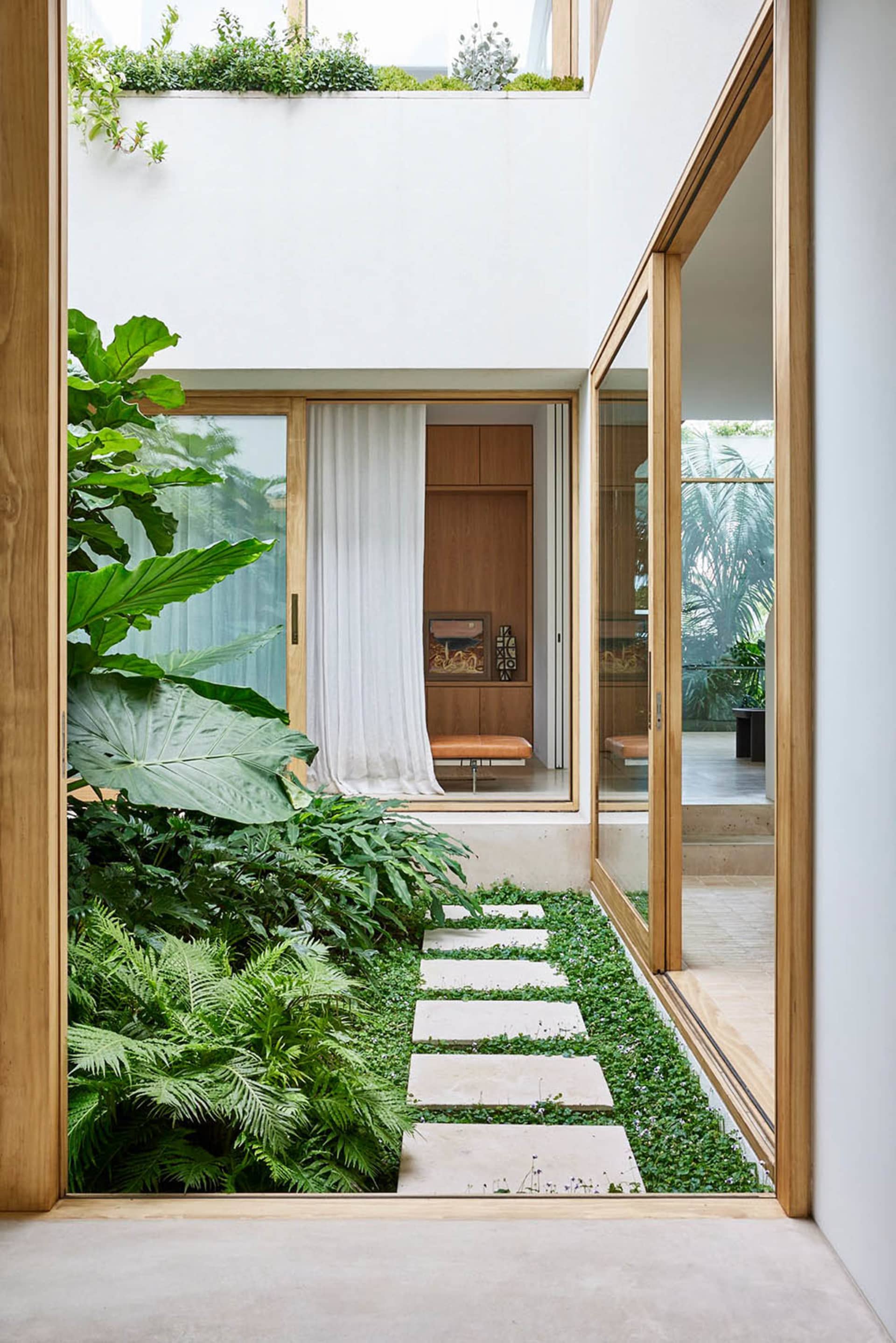 A modern indoor garden with wooden flooring, glass walls, and a pathway made of concrete tiles.