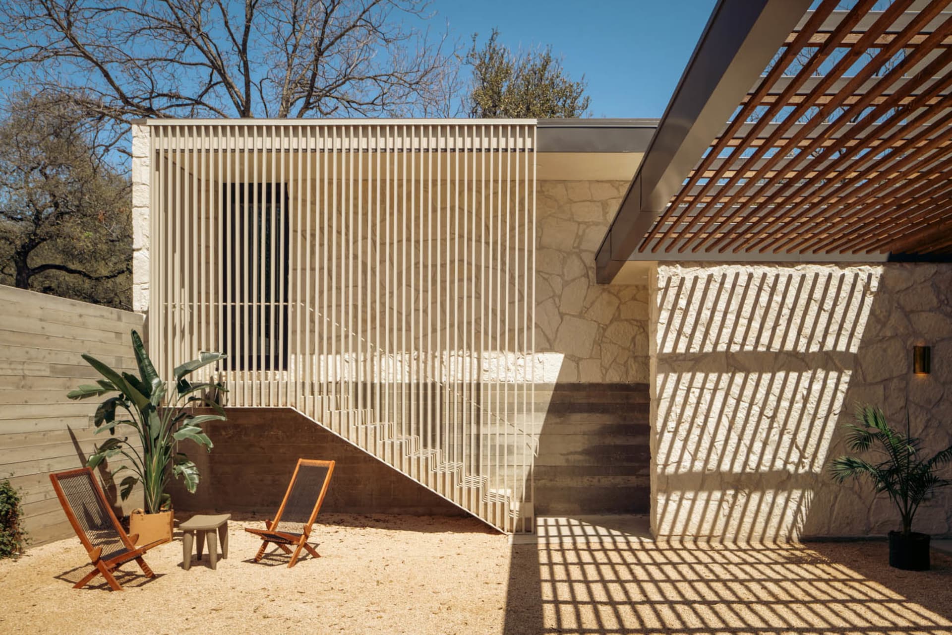 Modern residential entry featuring a wooden pergola, stone walls, and metal railings.
