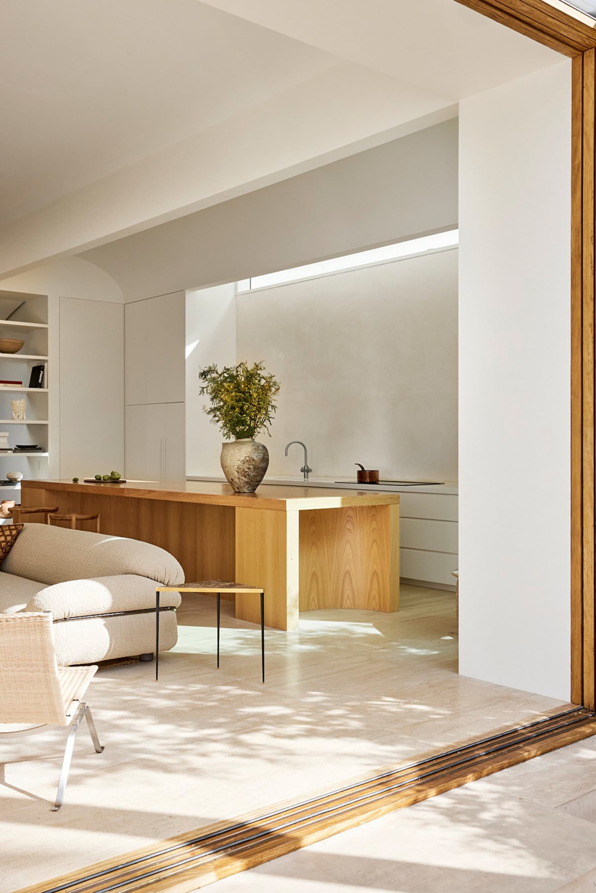 A minimalist residential interior with wood and marble materials, featuring a wooden island with a green plant and a marble s