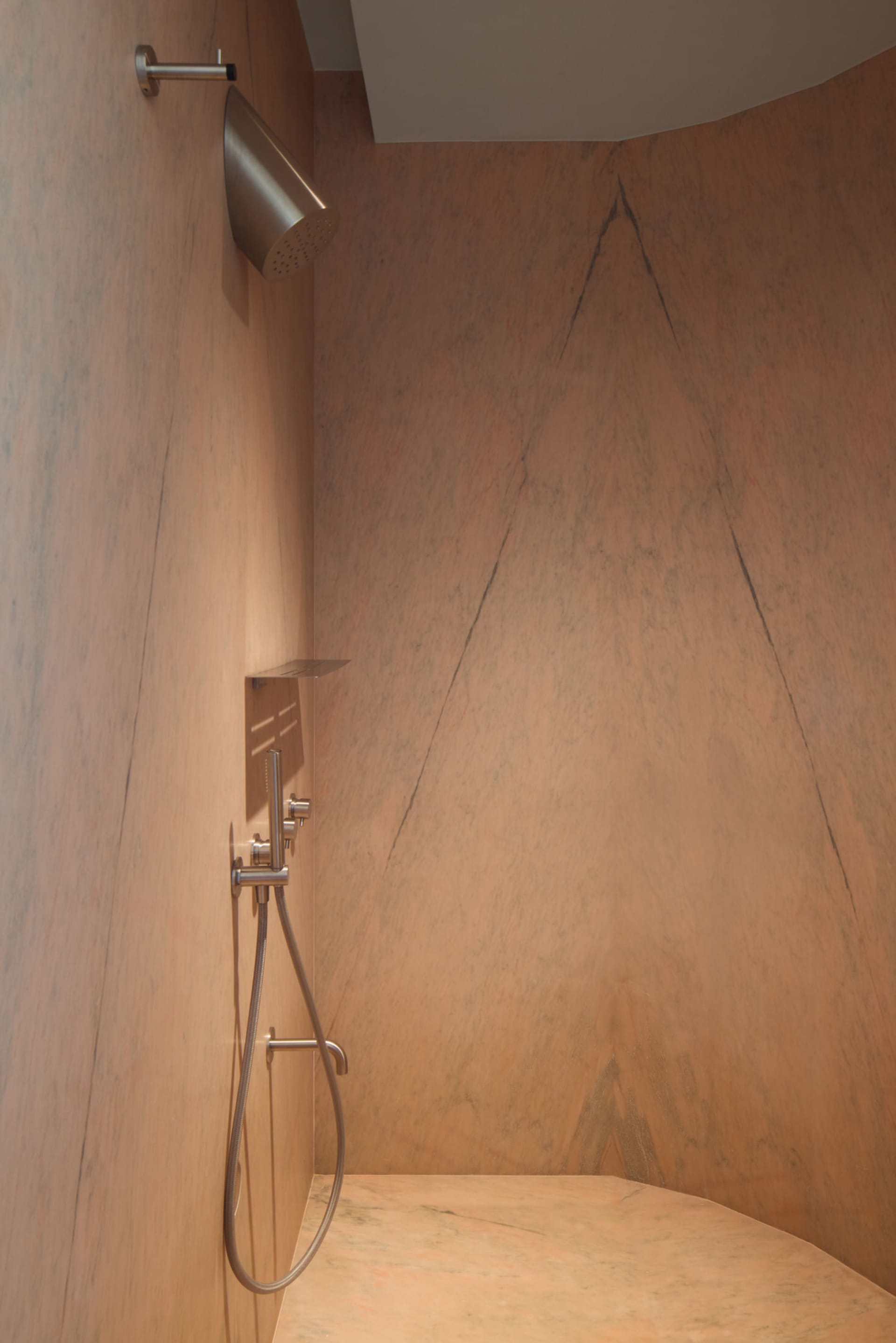 A minimalist bathroom with a sandstone wall and floor, featuring a modern shower head and fixtures.