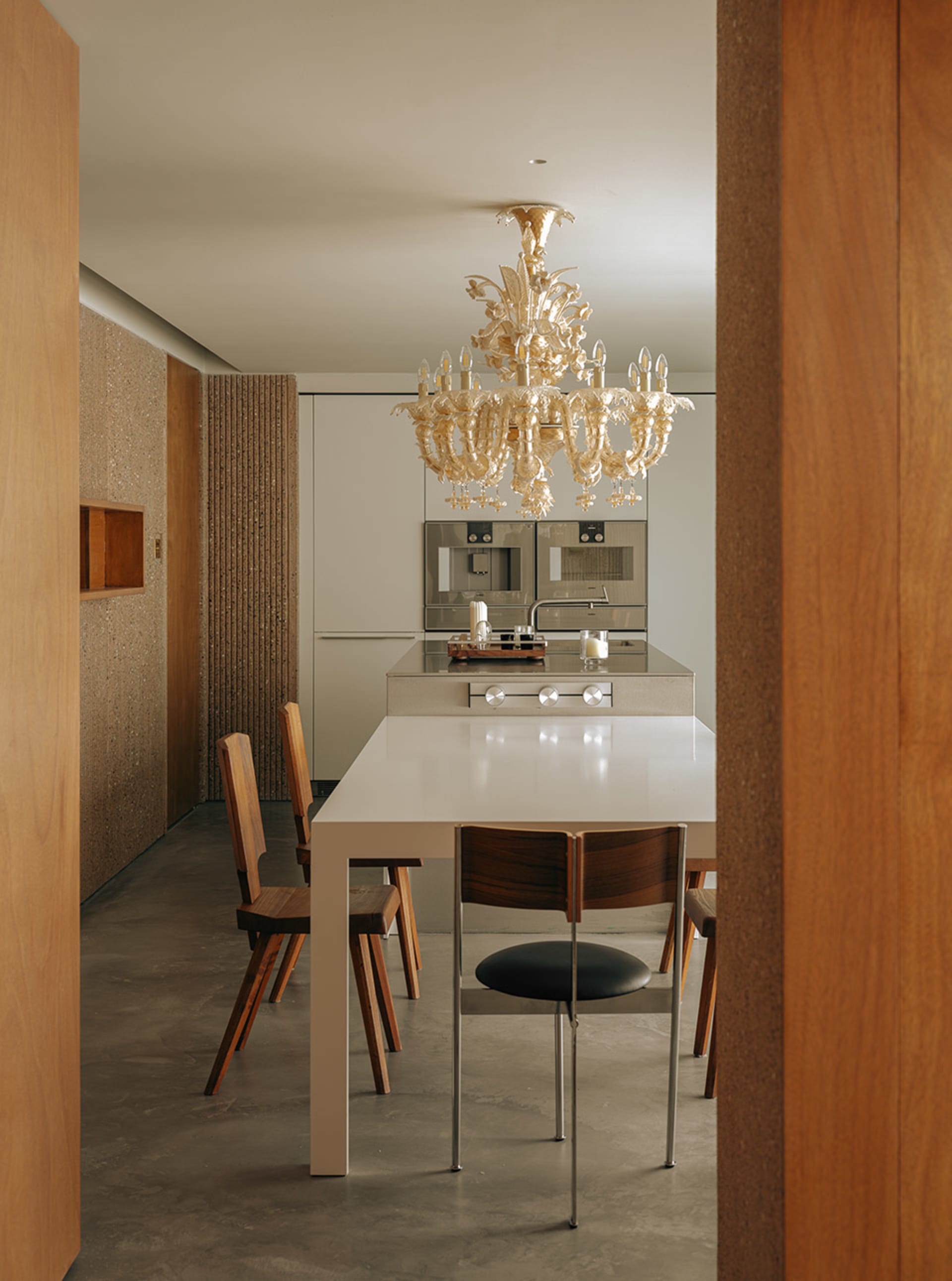 A modern kitchen and dining area featuring a metallic dining table and a crystal chandelier hanging above it.