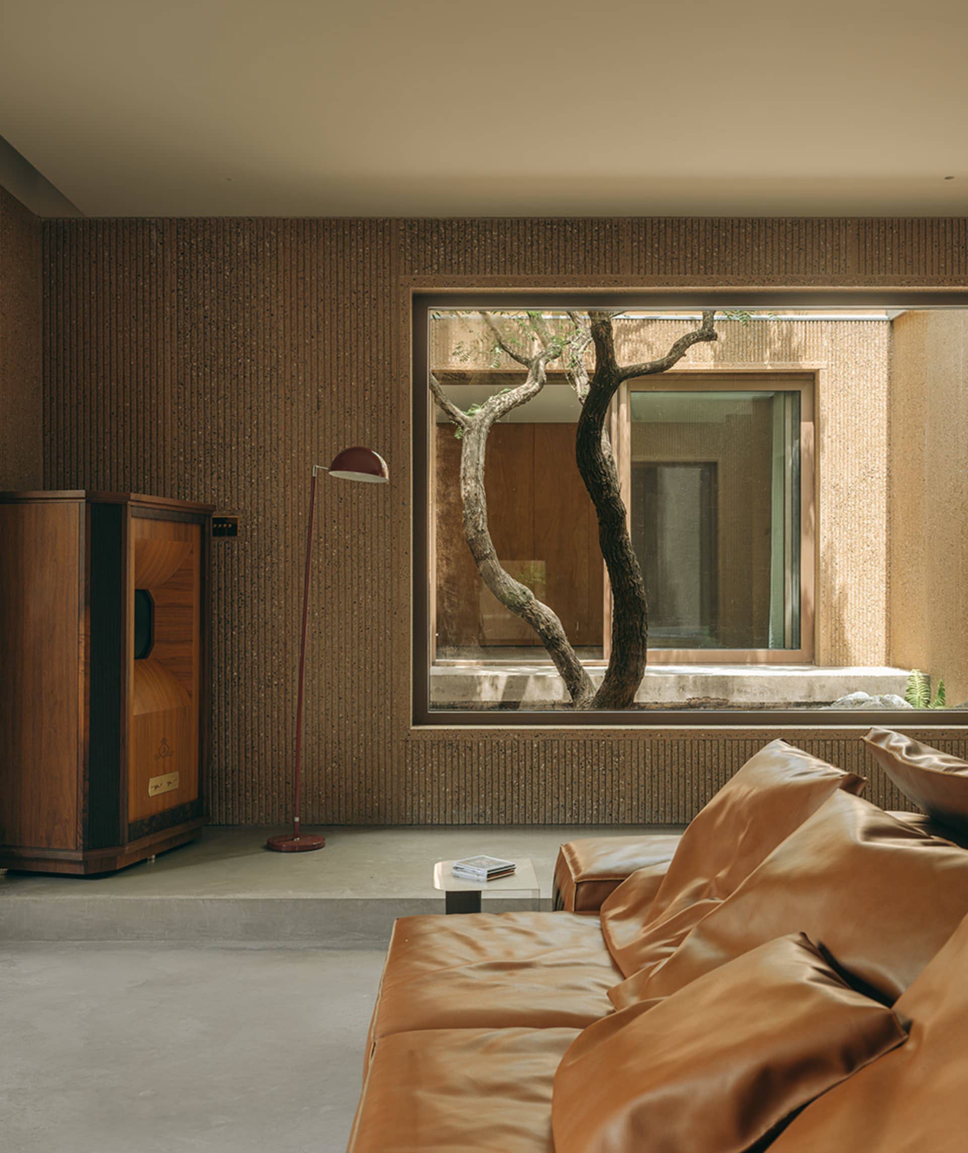 A modern living room with a textured concrete wall, a brown leather sofa, and a floor lamp with a red shade.